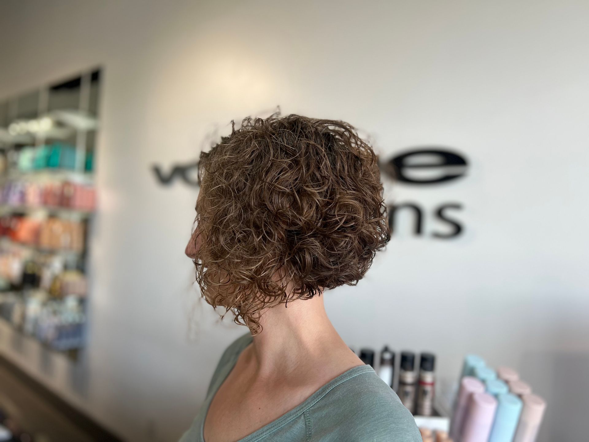 A woman with curly hair is standing in a salon.