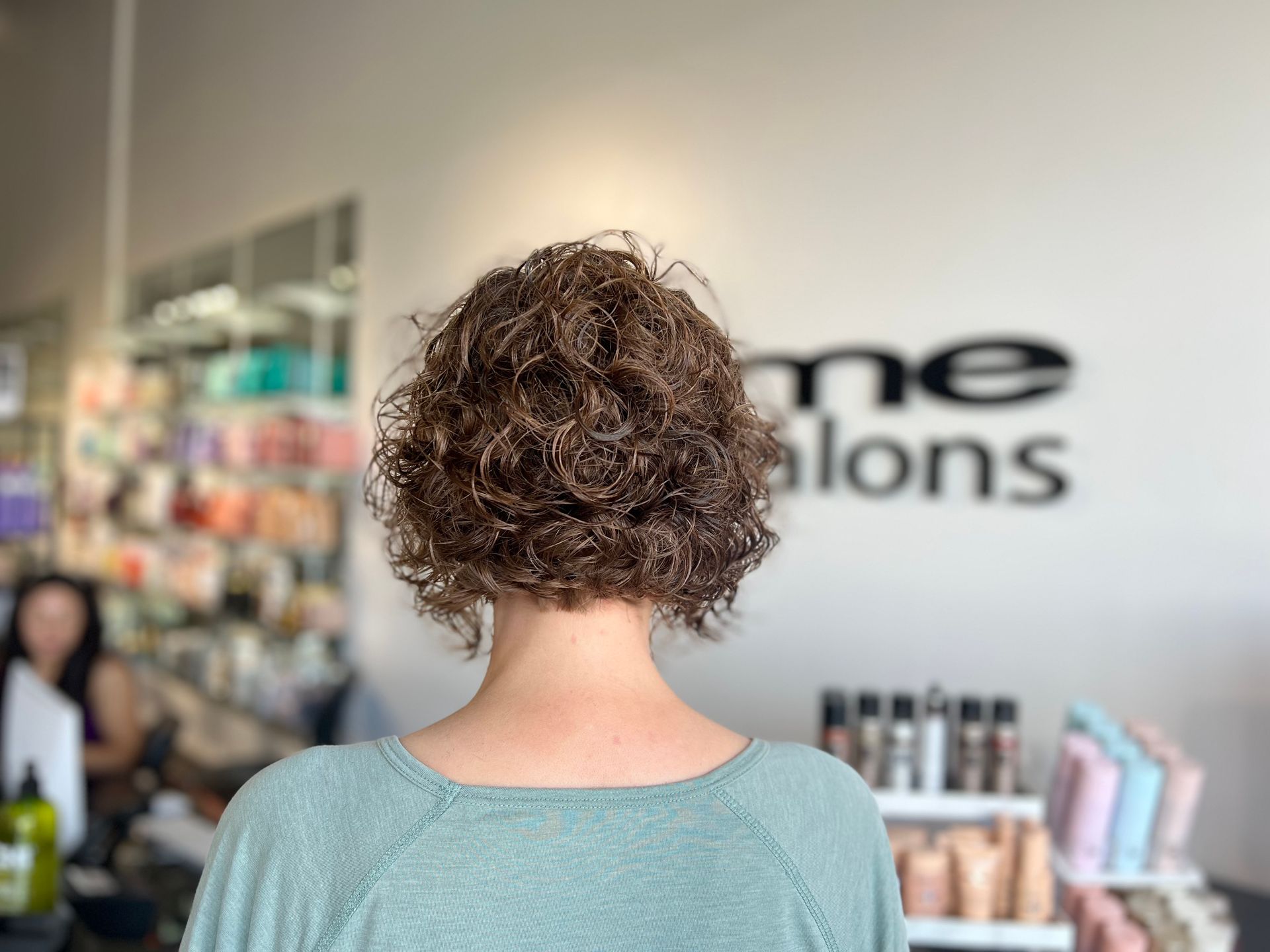 A woman with curly hair is standing in a salon.