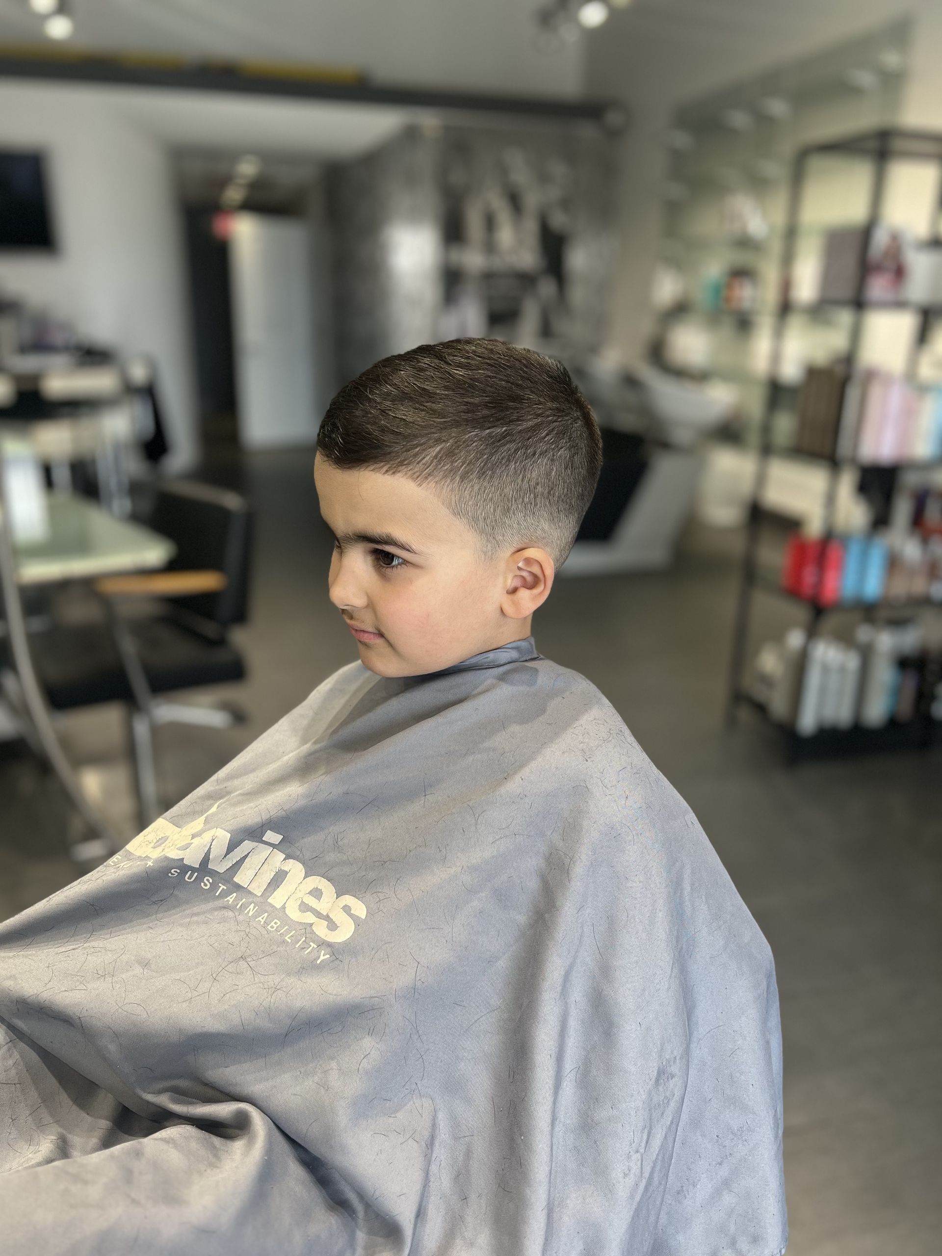 Boy with freshly cut hair in a salon, wearing a barber cape.