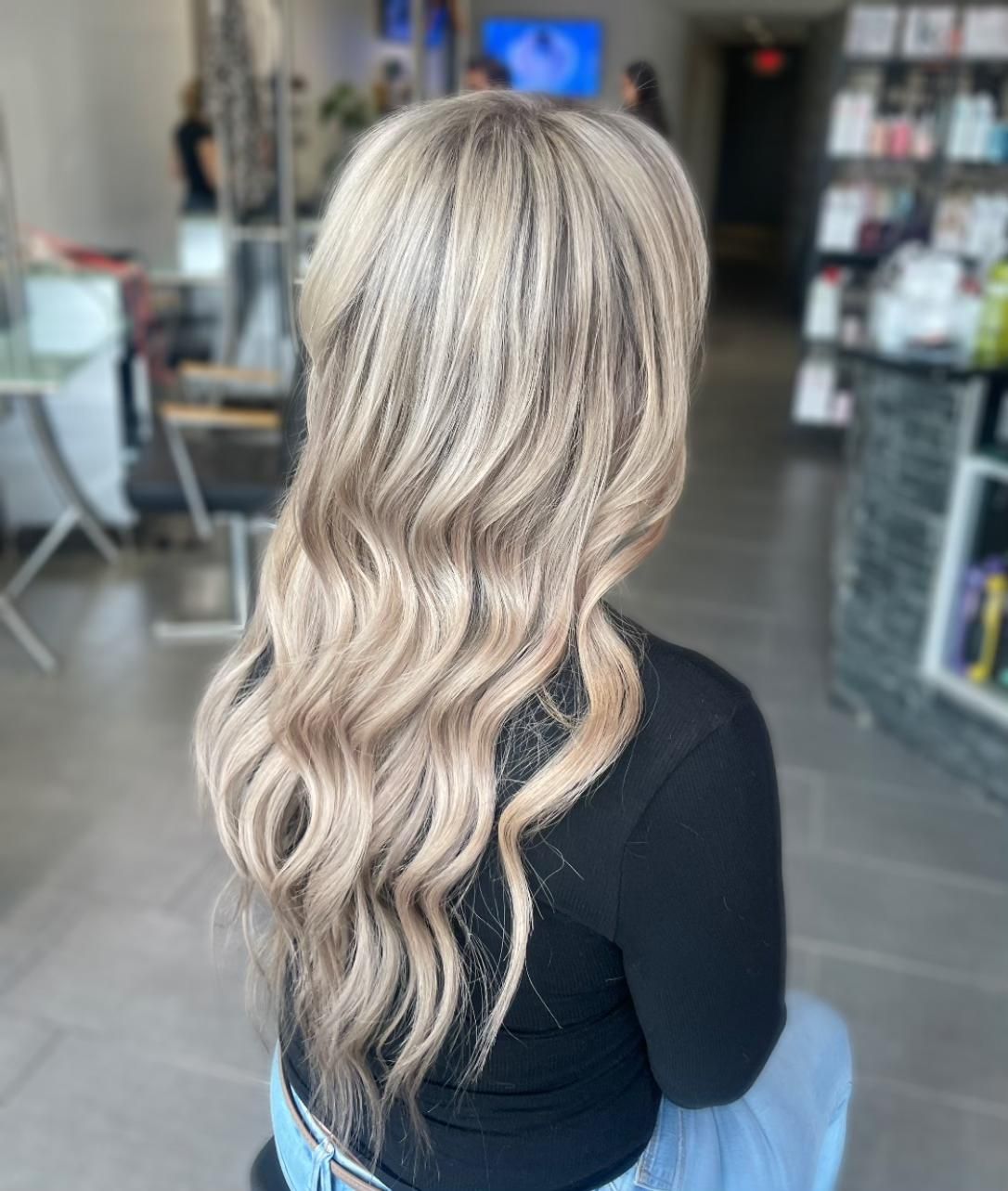 A woman with long blonde hair is sitting on a stool in a salon.