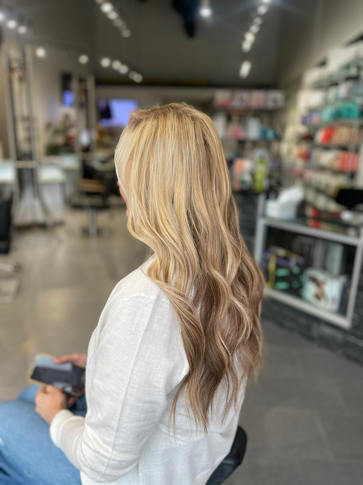 A woman with long blonde hair is sitting on a stool in a salon.