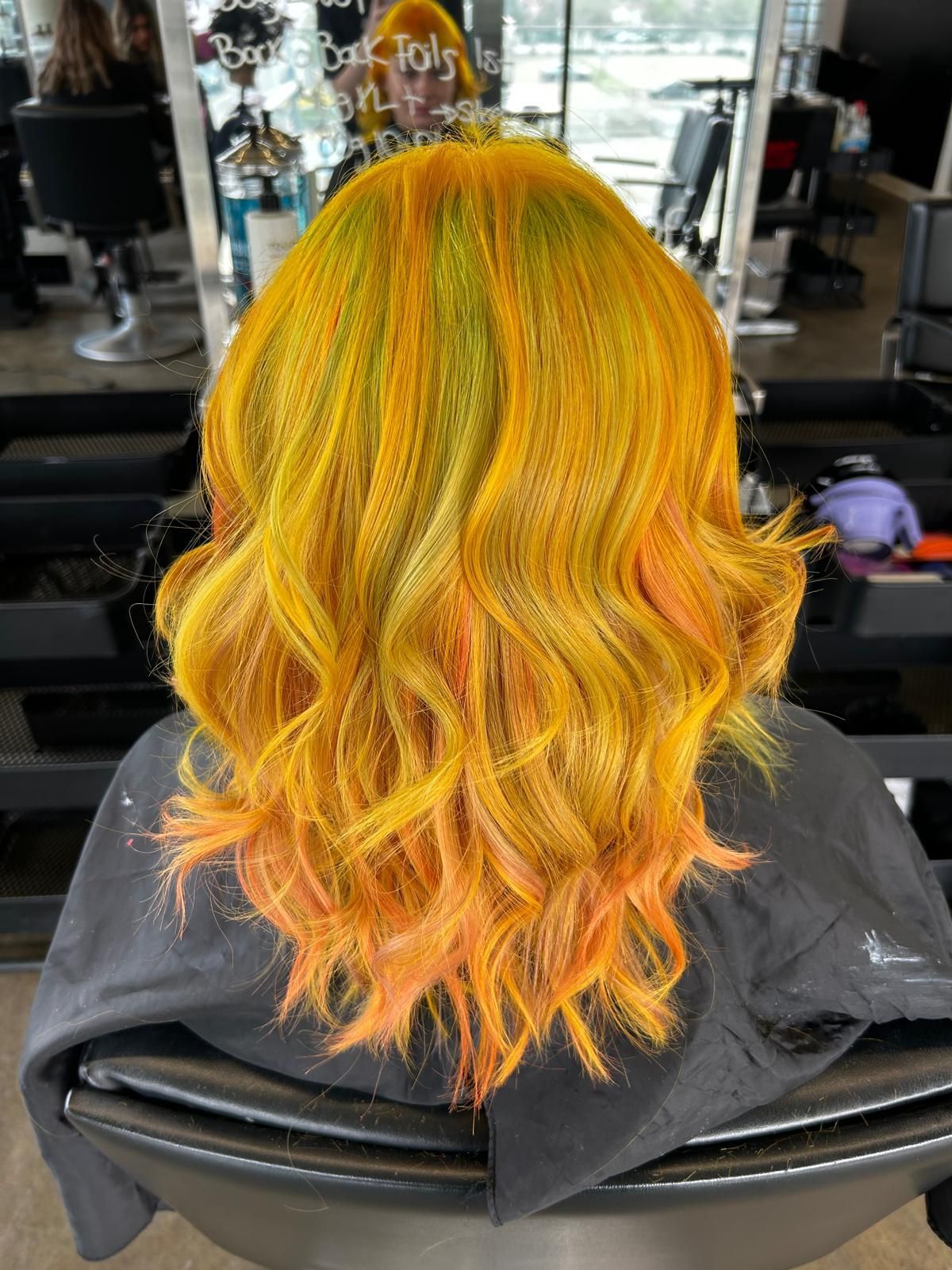 A woman with bright yellow hair is sitting in a chair in a salon.