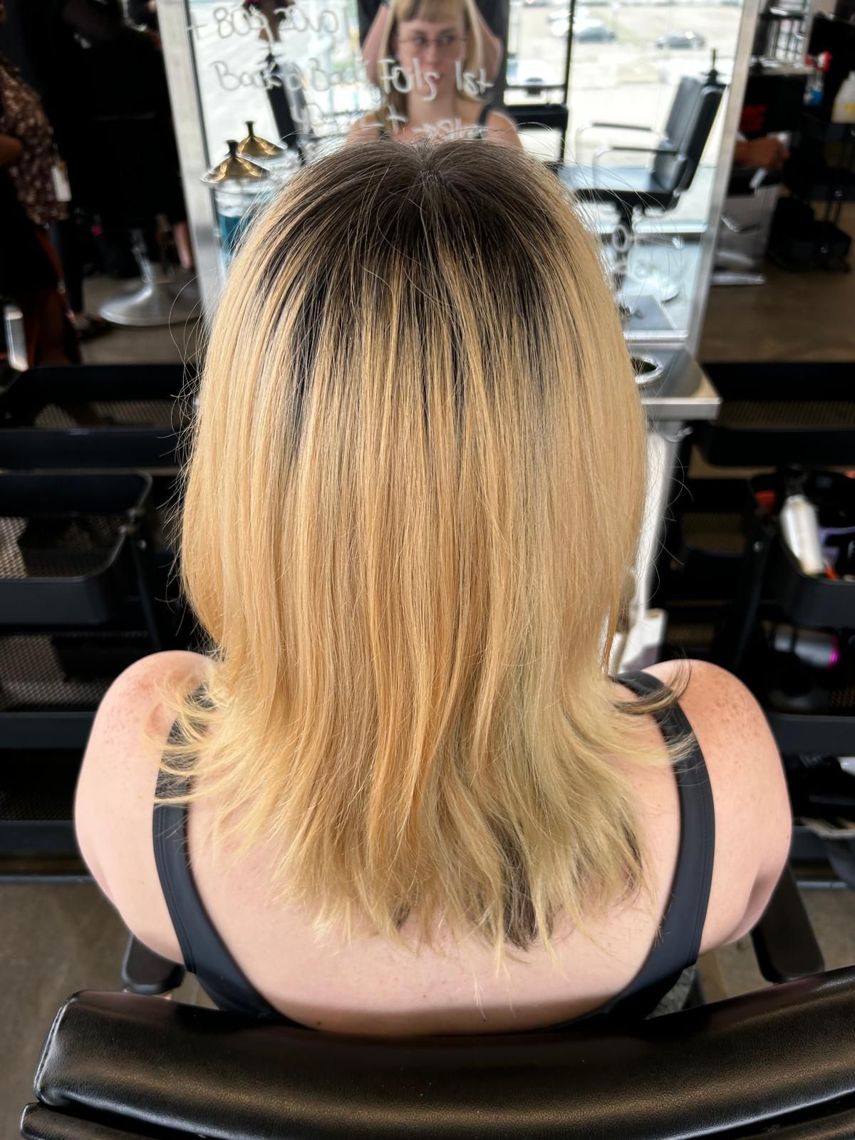 A woman with blonde hair is sitting in a chair in front of a mirror.