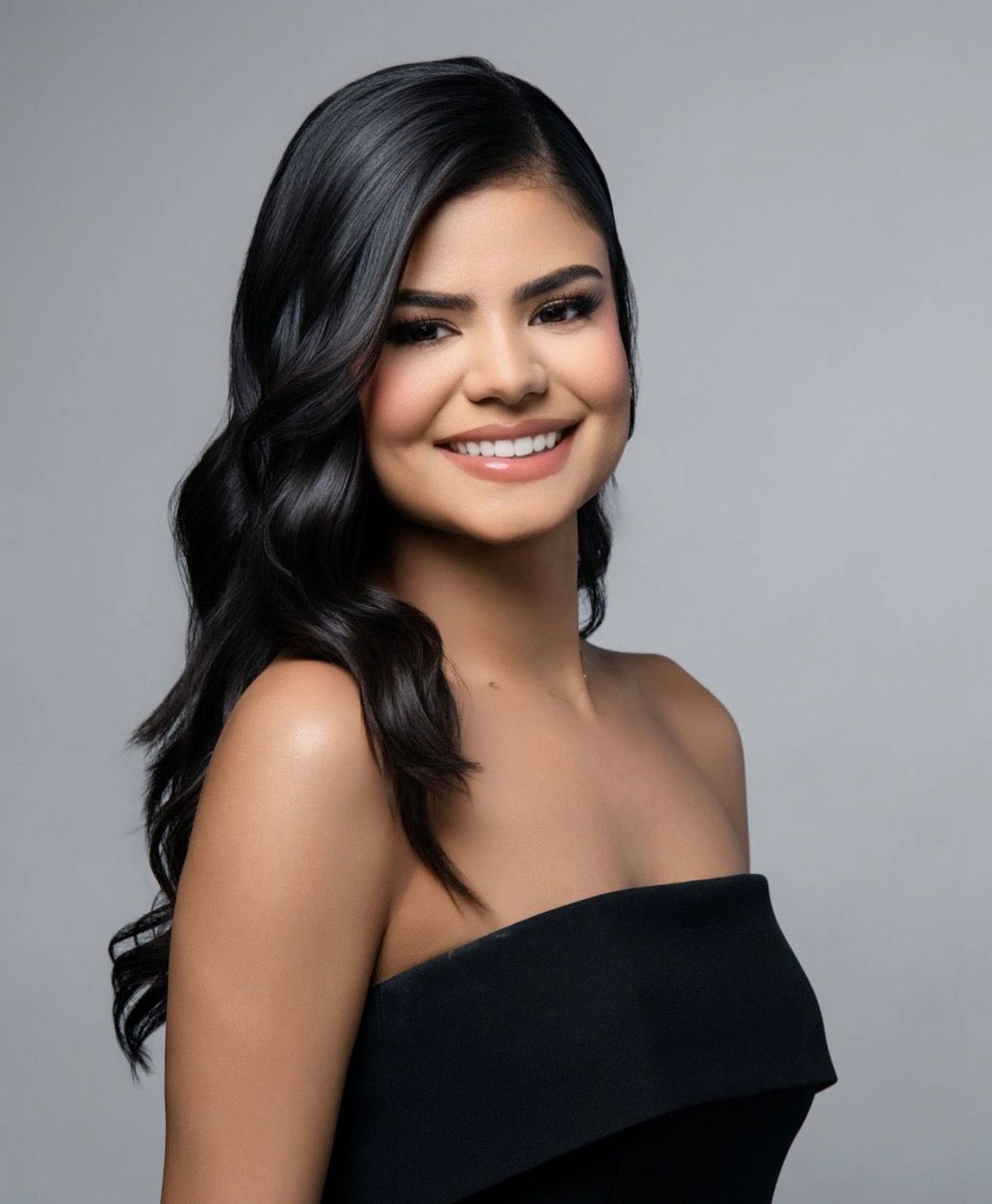 A woman in a black off the shoulder top smiles for the camera