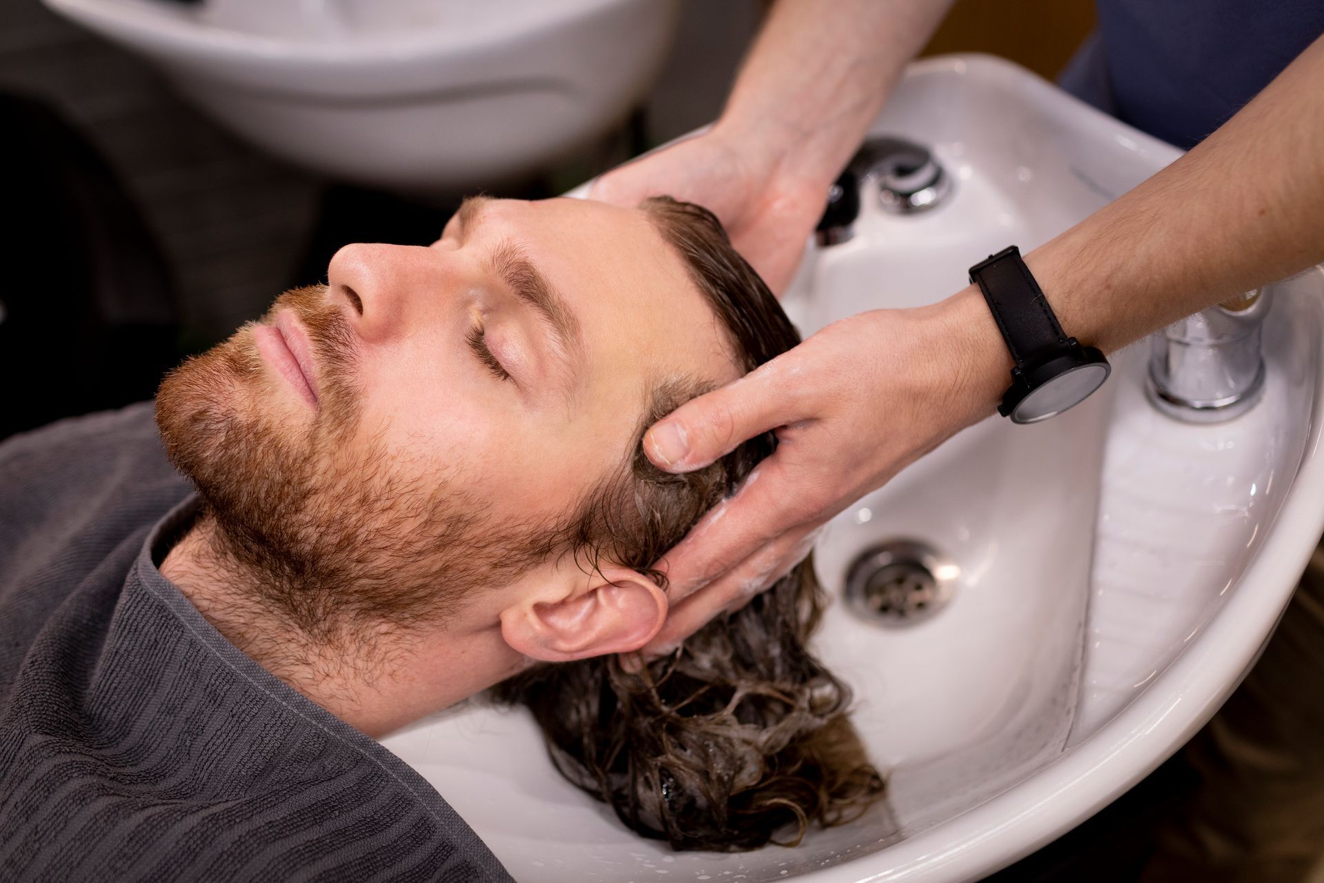 A man is getting his hair washed in a sink at a hair salon.