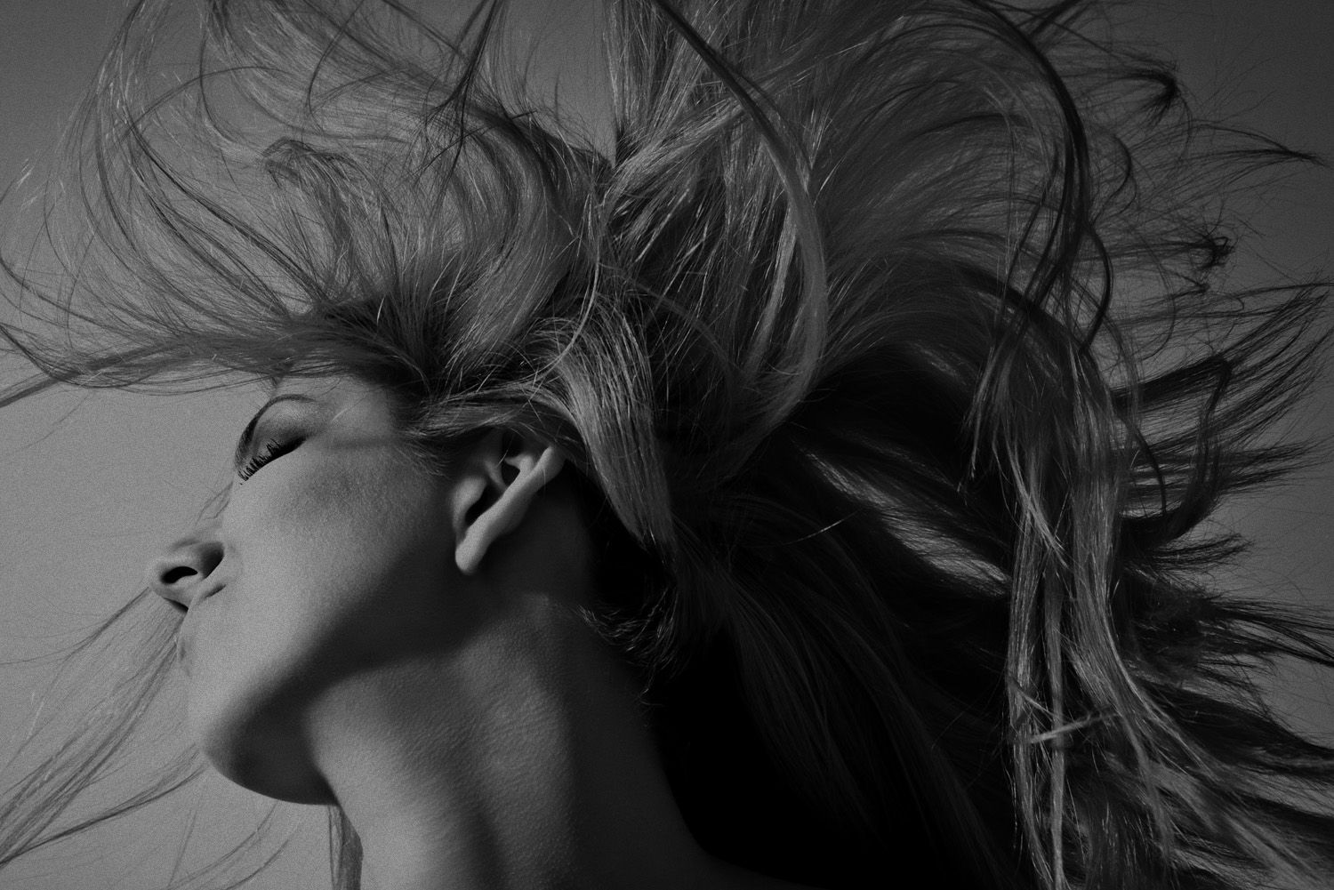 a black and white photo of a woman with her hair blowing in the wind .