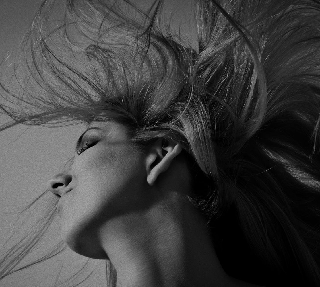 a black and white photo of a woman with her hair blowing in the wind .