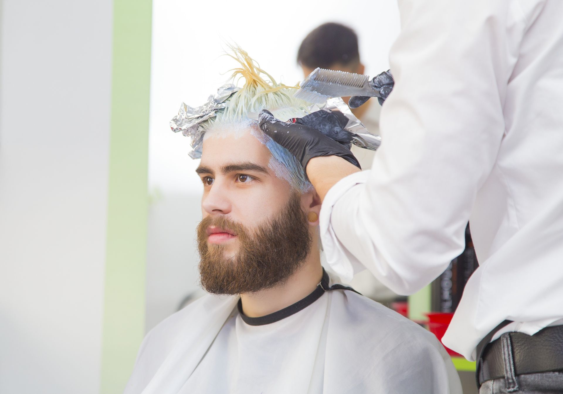 a man with a beard is getting his hair dyed by a hairdresser .