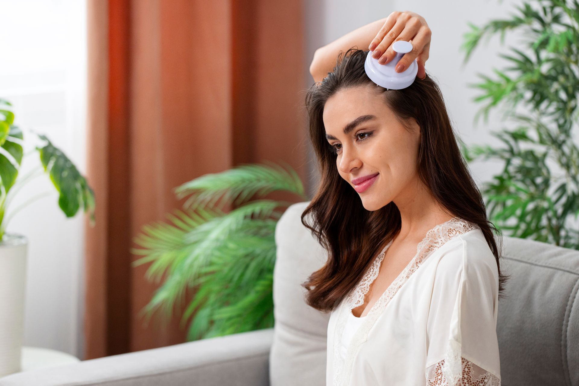 A woman is brushing her hair while sitting on a couch.