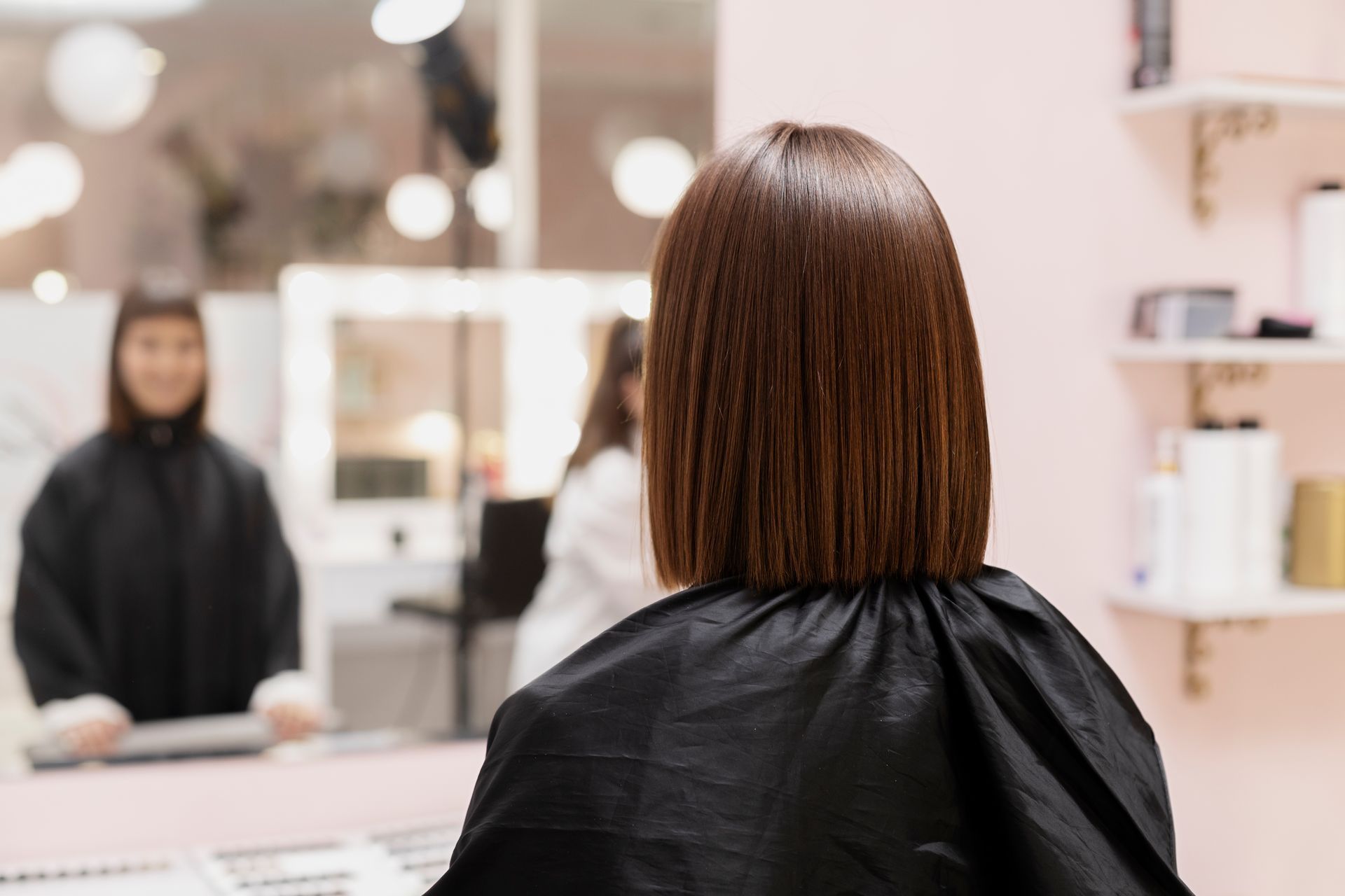 A woman is sitting in front of a mirror at a hair salon.