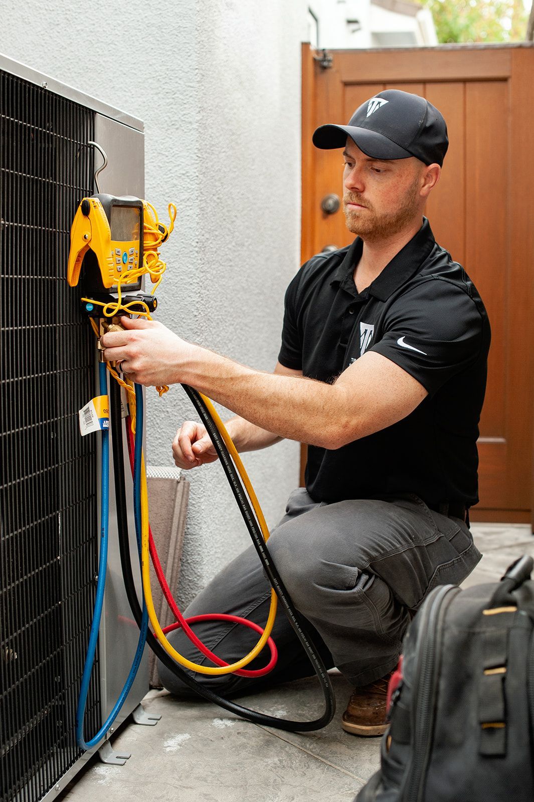 HVAC technician kneels, using gauges to service an outdoor air conditioning unit.