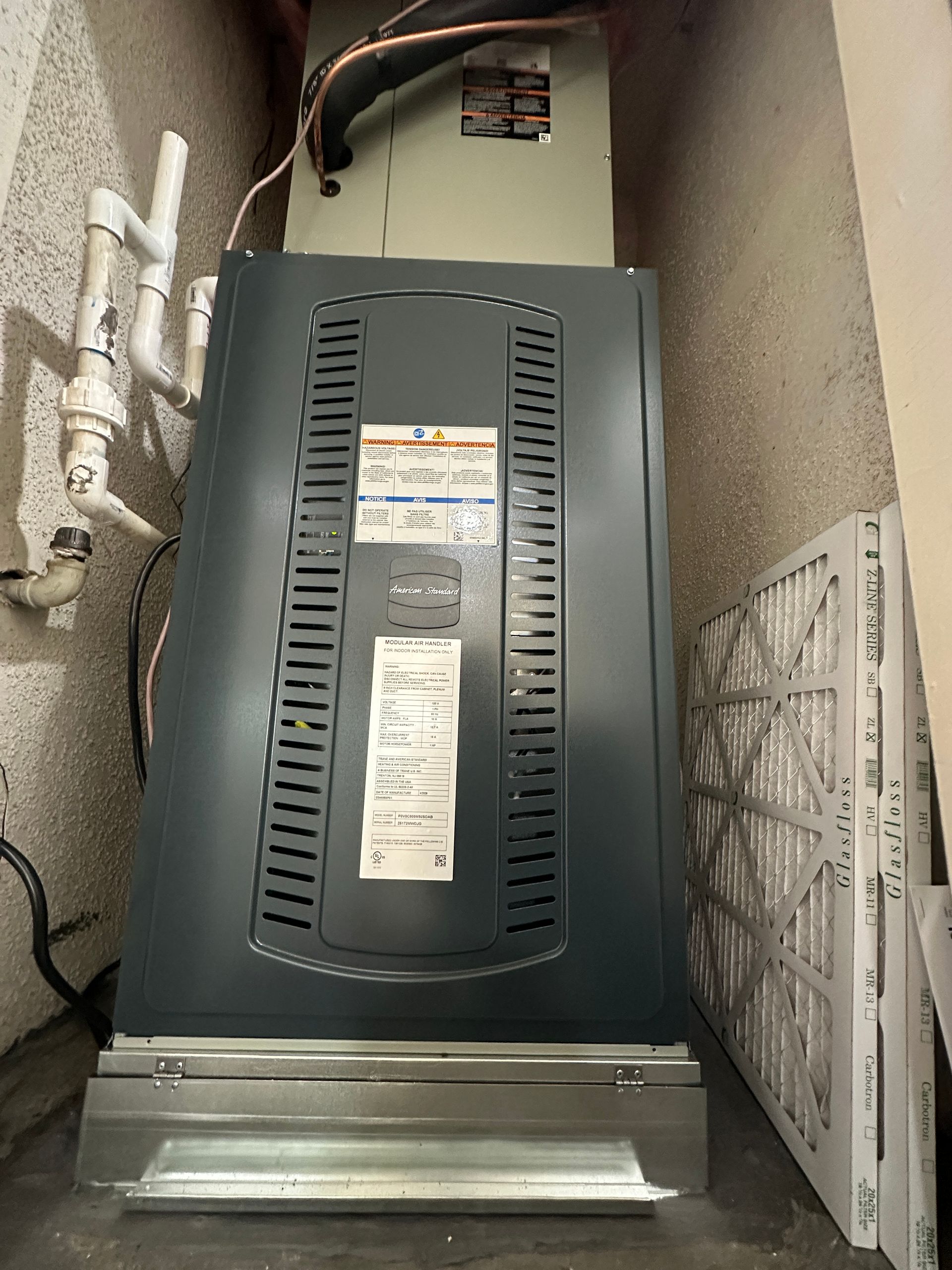Furnace unit in a corner, with replacement air filters stacked to the side. Gray and white.