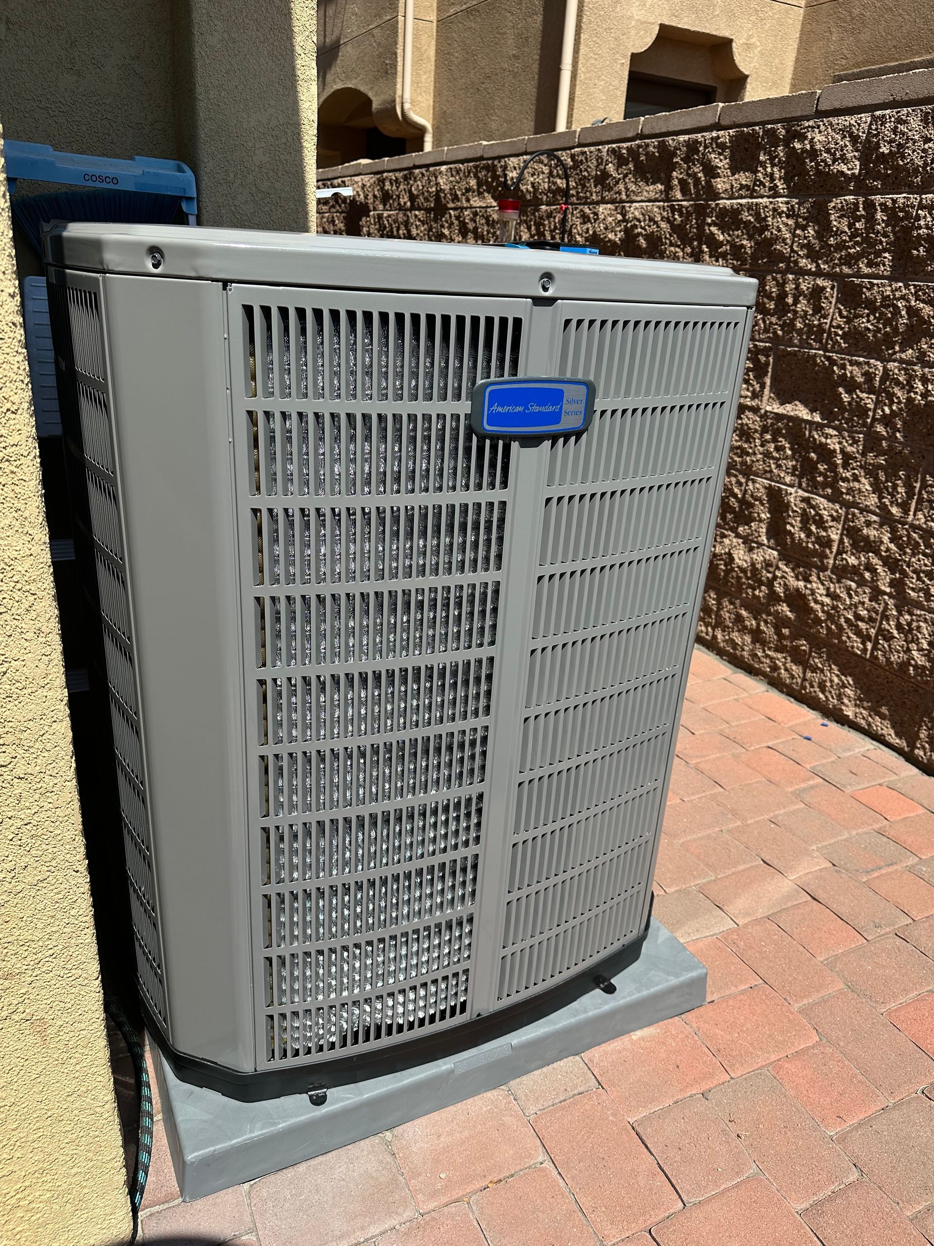 Air conditioning unit on a concrete pad, next to a textured brick wall and a light-colored wall.