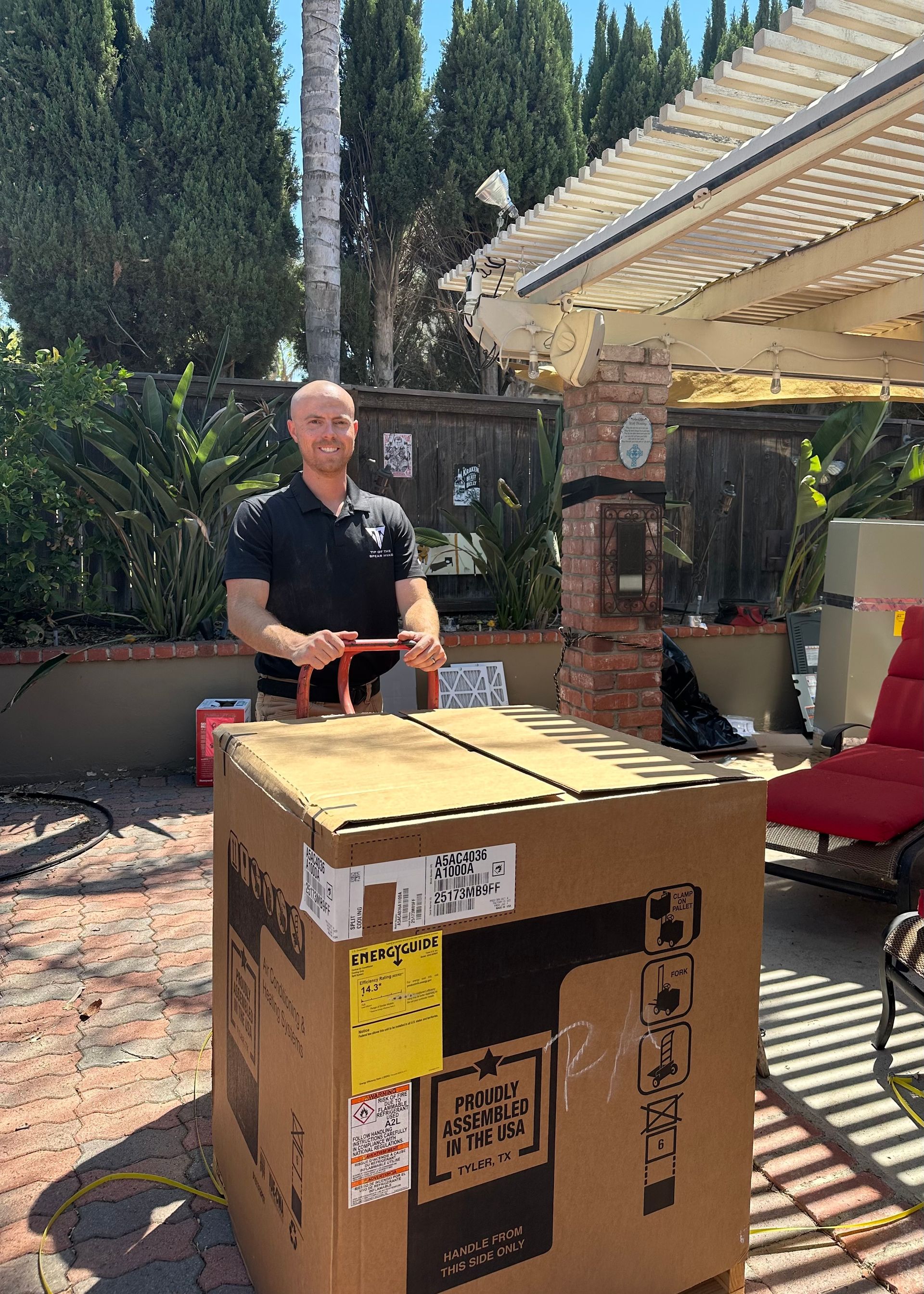 Man pushing large cardboard box outdoors. Sunny day, patio setting.