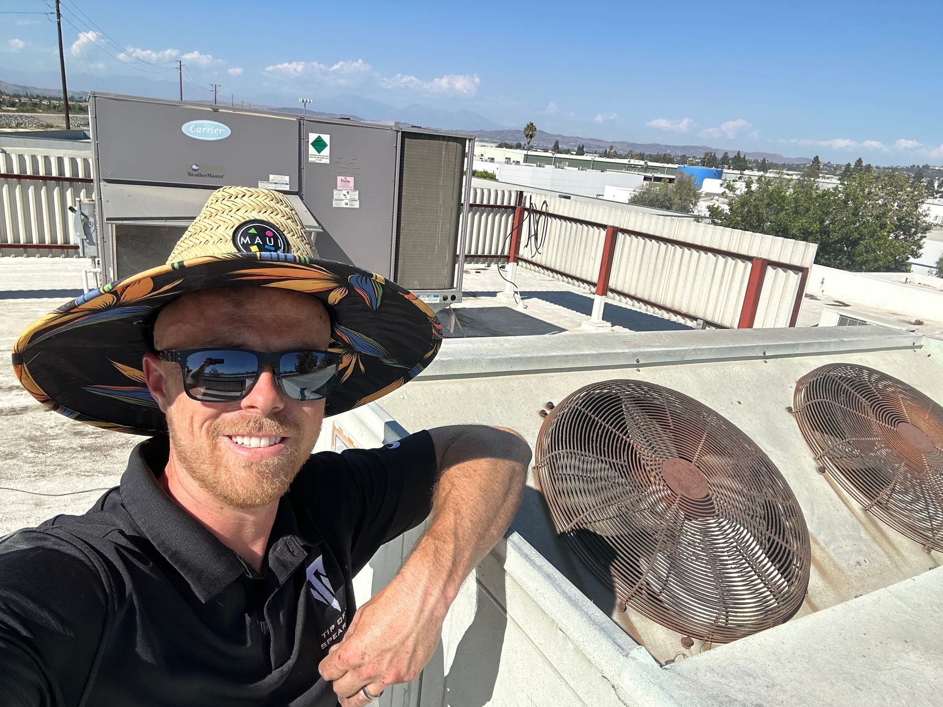 Man on a rooftop wearing a hat and sunglasses, smiling near HVAC equipment, sunny day.