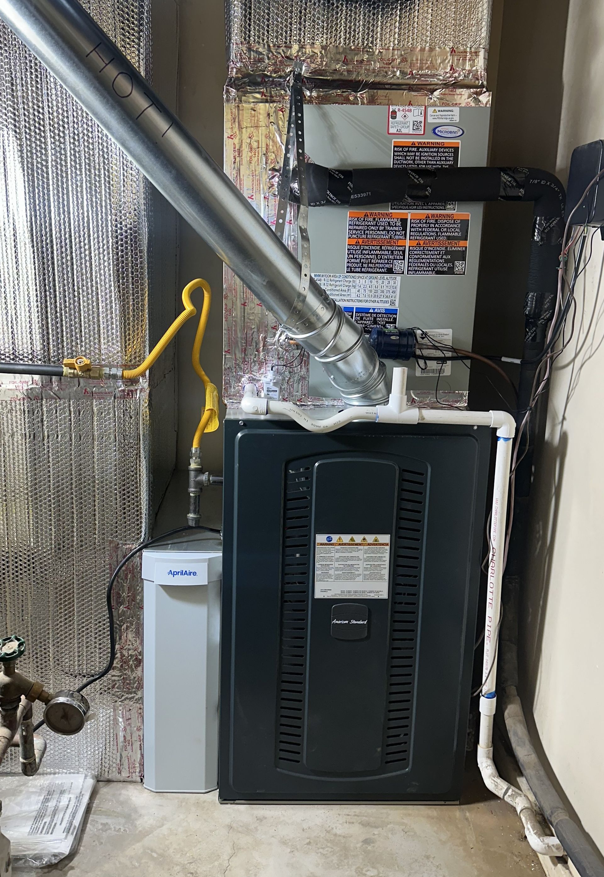 Furnace and water softener in a basement, with silver ductwork, gray components, and reflective insulation.