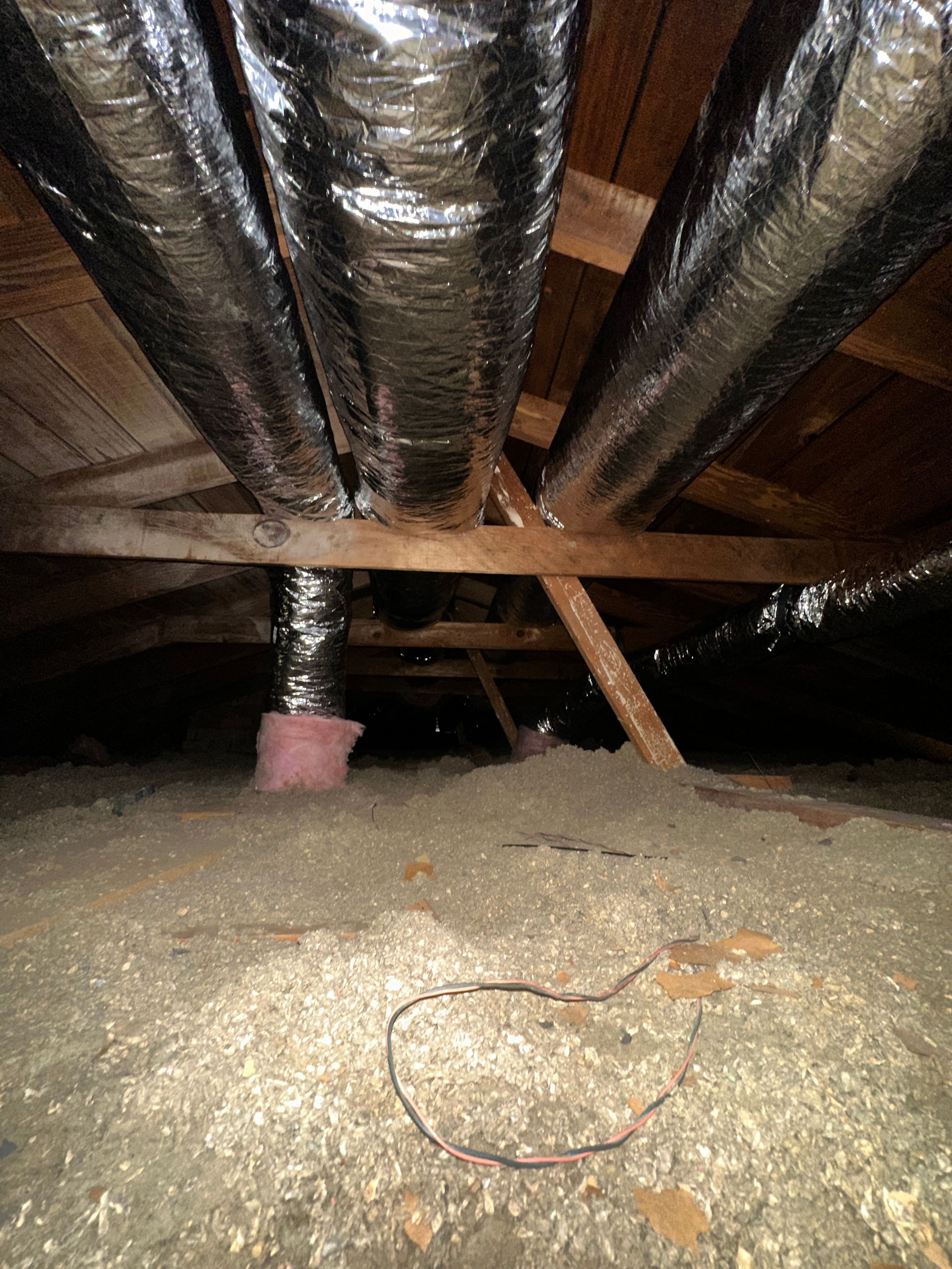 Attic with ductwork and insulation; a pink piece of insulation hangs down.