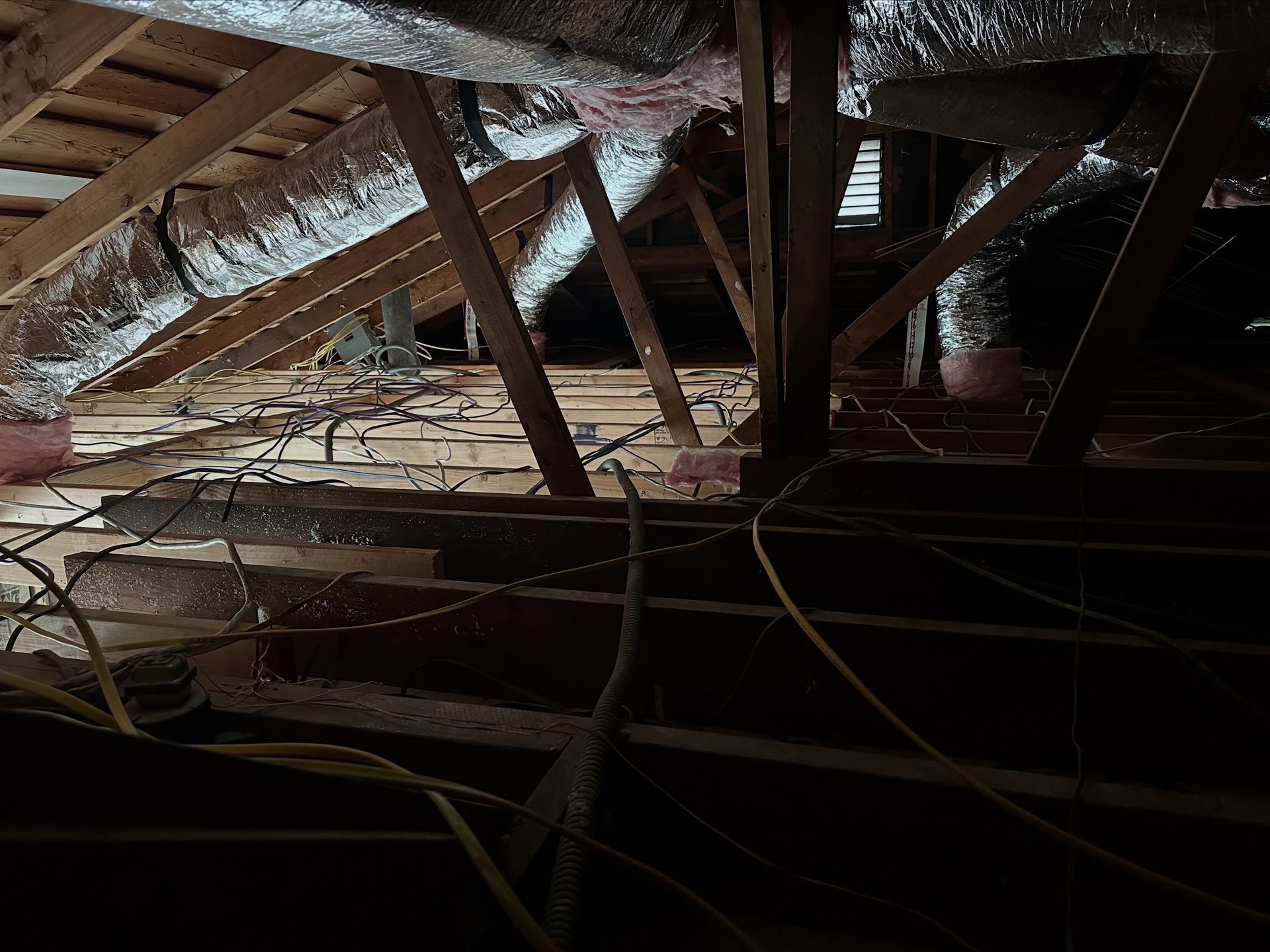 Interior view of an attic with wooden beams, insulation, and electrical wiring.