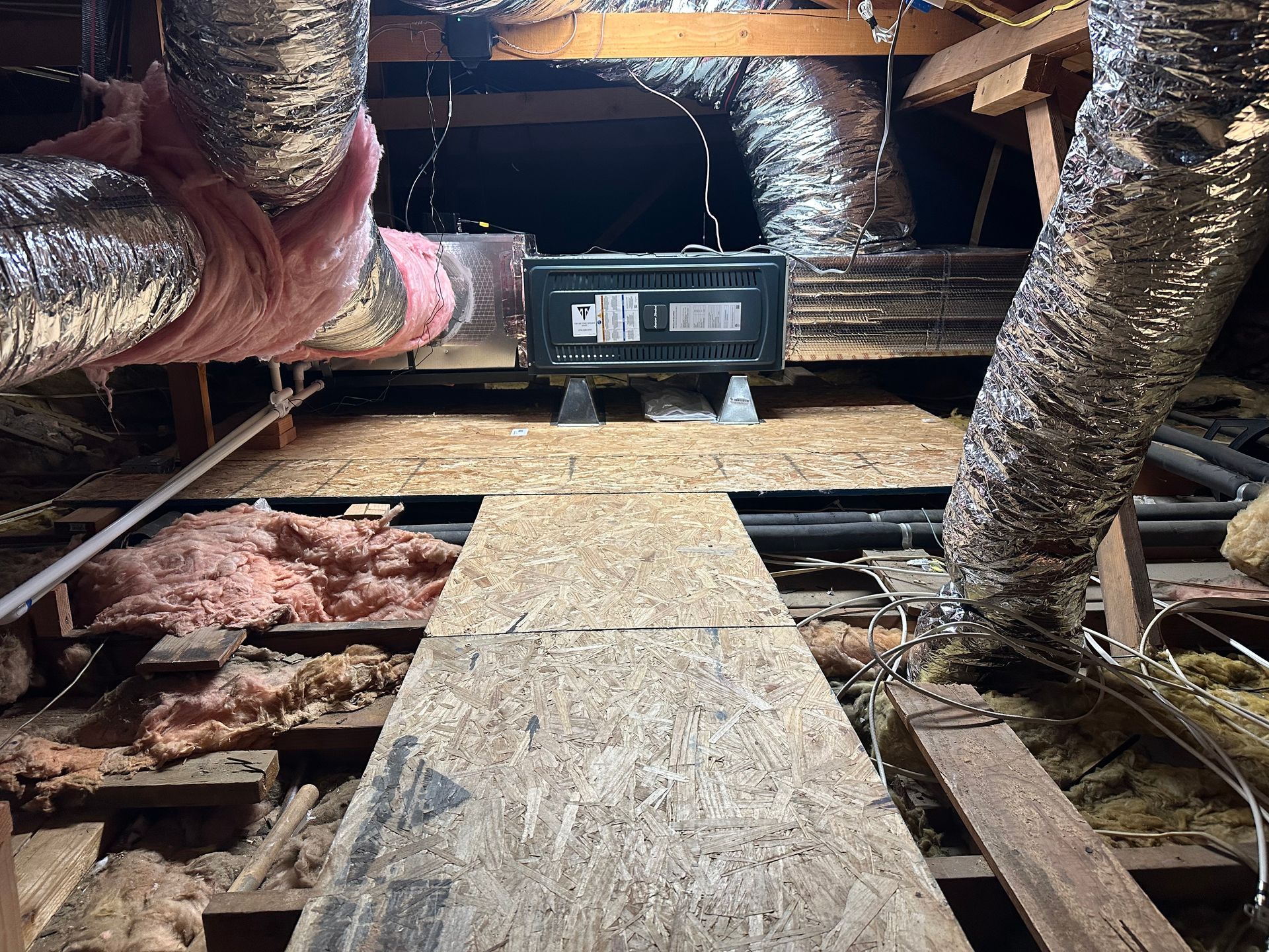 Attic with HVAC unit, ductwork, insulation, and wooden walkway.