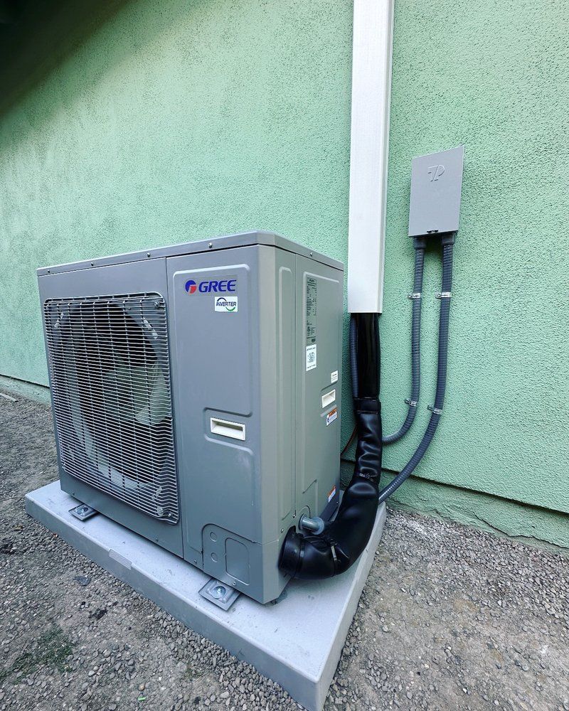 Tip of the Spear HVAC  | a gray air conditioner is sitting on the side of a green building.