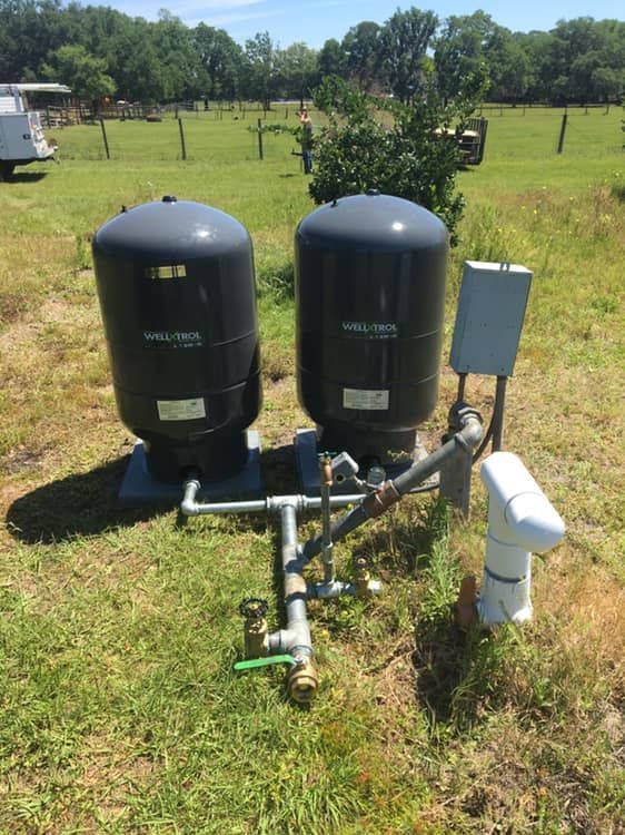 Two black water tanks are sitting in a grassy field