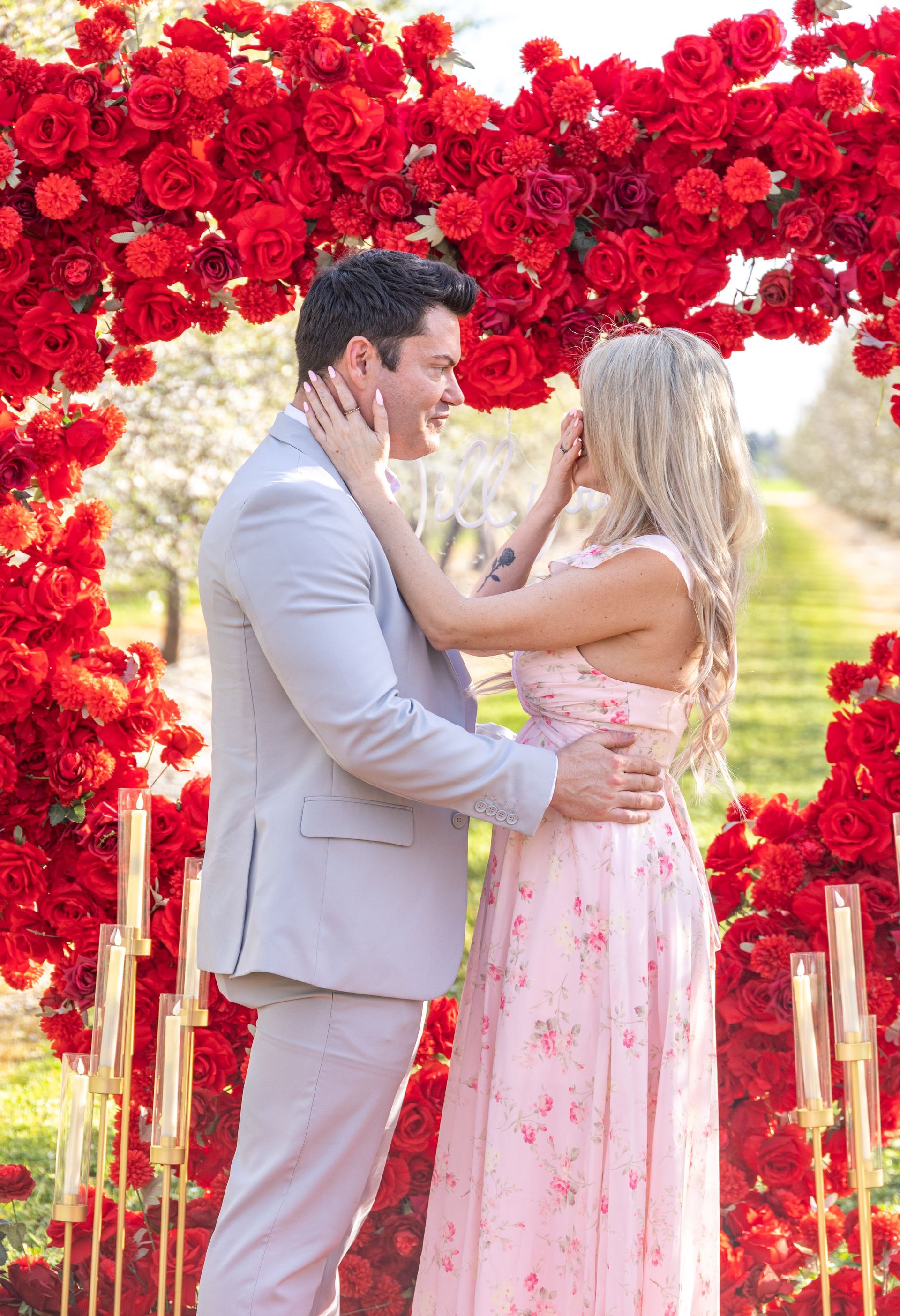 Young person embraces a smiling person in a blossoming orchard. Both are looking at the camera.