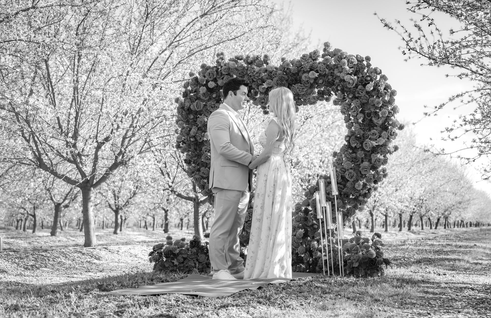 Couple embracing, noses touching, near a red building. Woman in white dress, man in brown jacket.