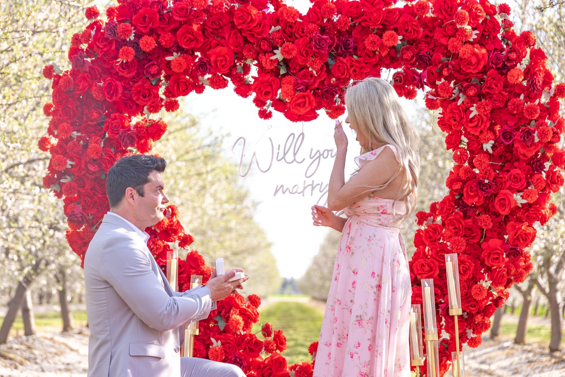 Couple kissing outdoors near palm trees. Man in black shirt, woman in red dress.