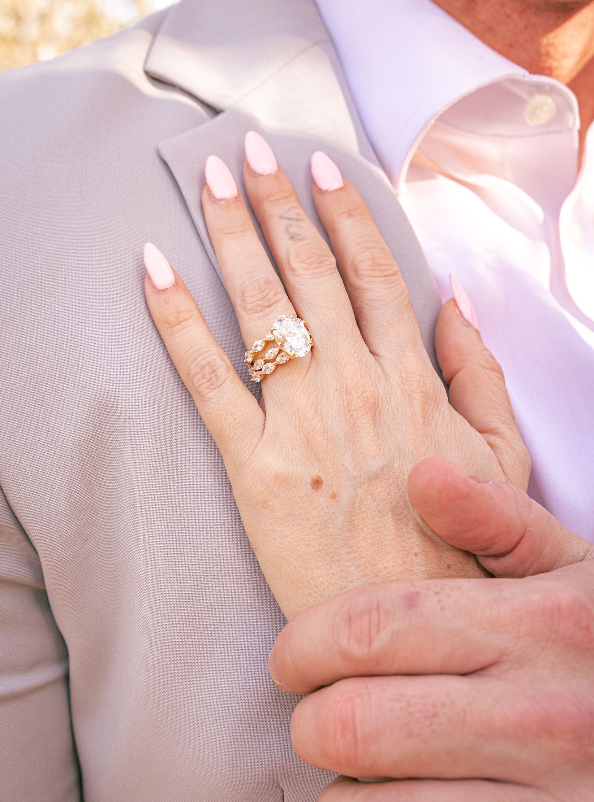 Couple leans in close, about to kiss. Man wears blue shirt, woman a red dress, in front of flowering tree.