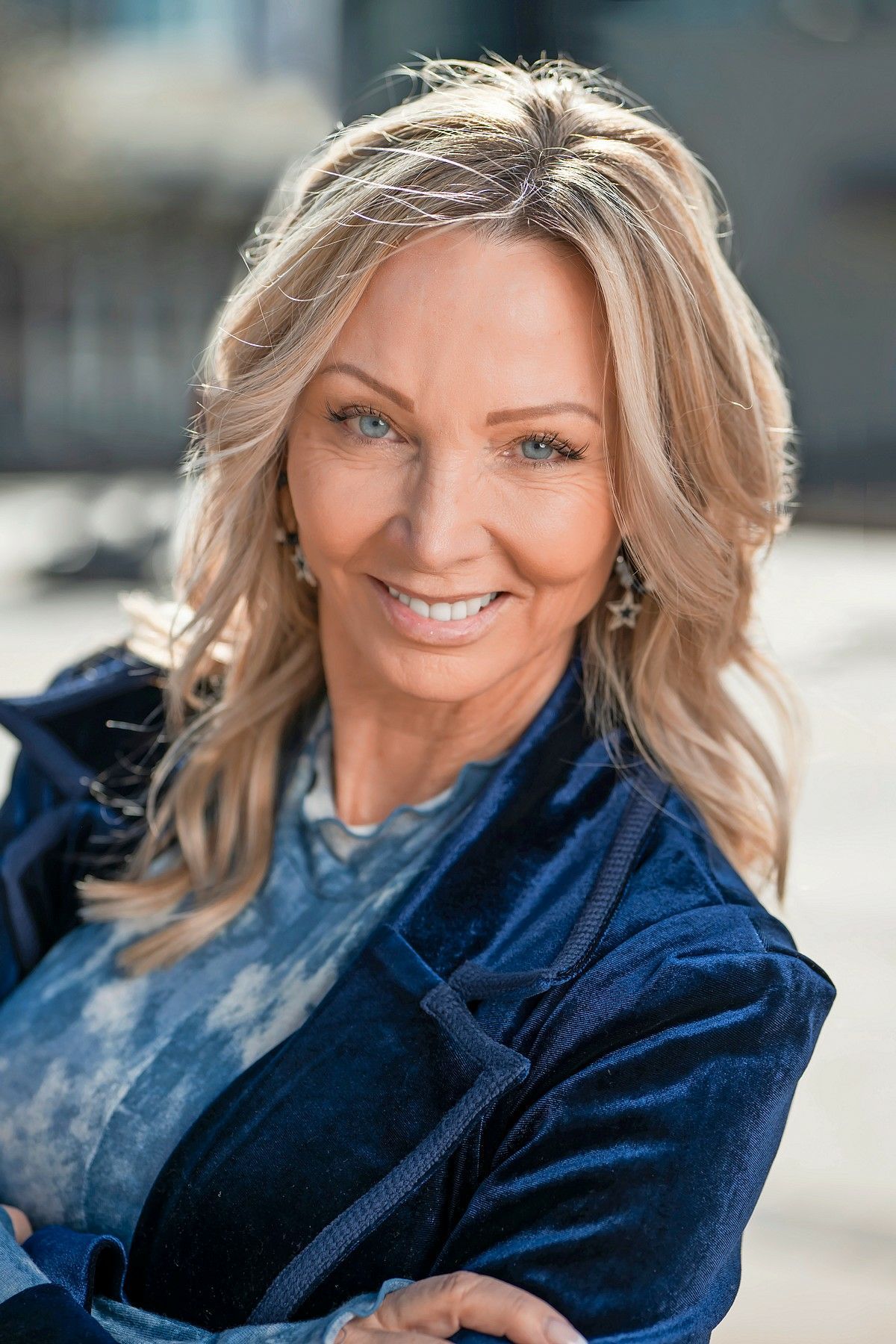 Woman with blonde hair wearing a blue jacket smiles outside.