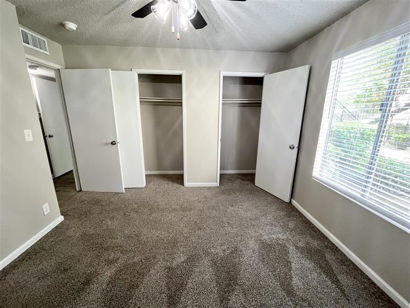Empty bedroom with two closets, a window with blinds, and beige walls.