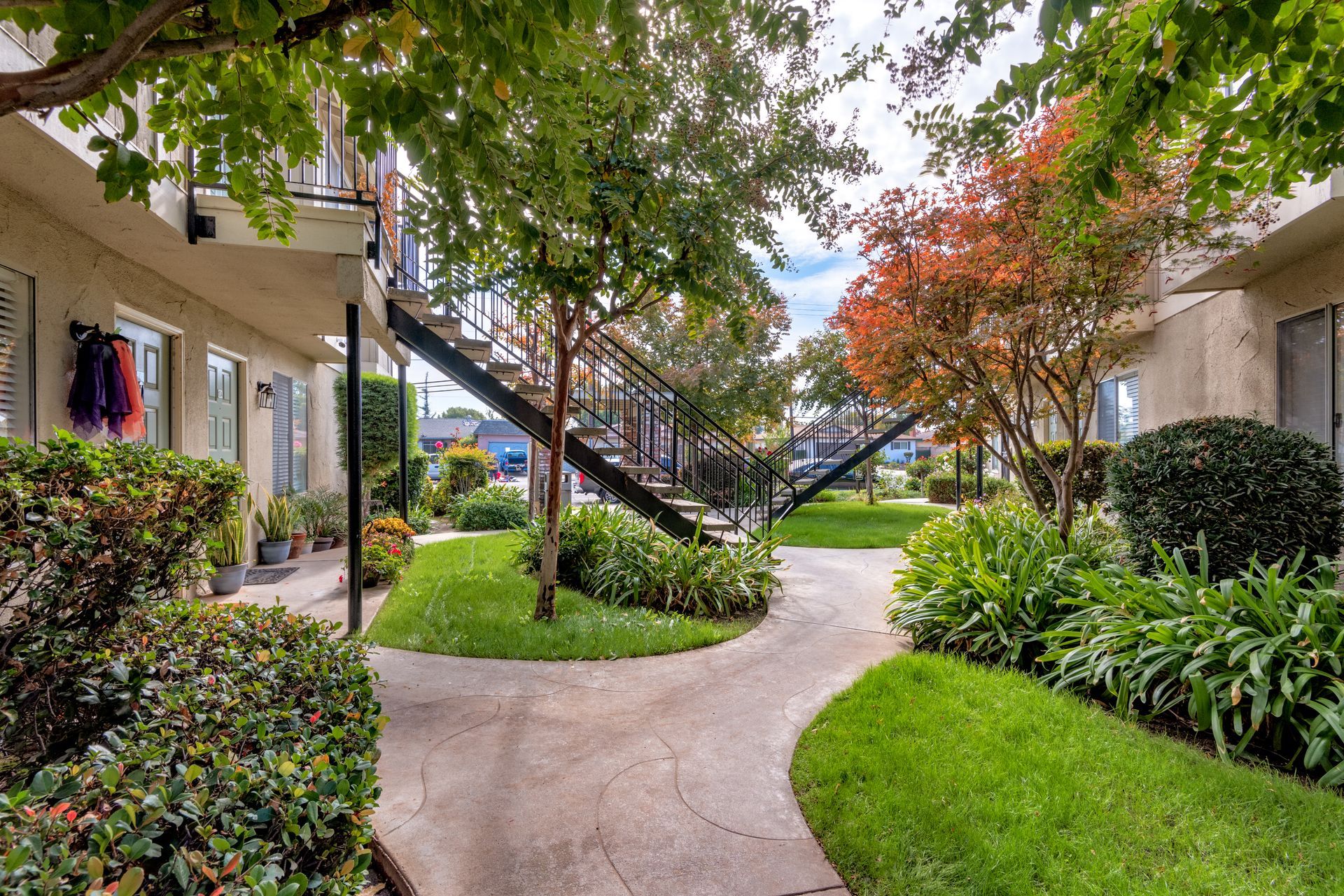 Apartment complex courtyard with walkways, greenery, trees, and two-story buildings.