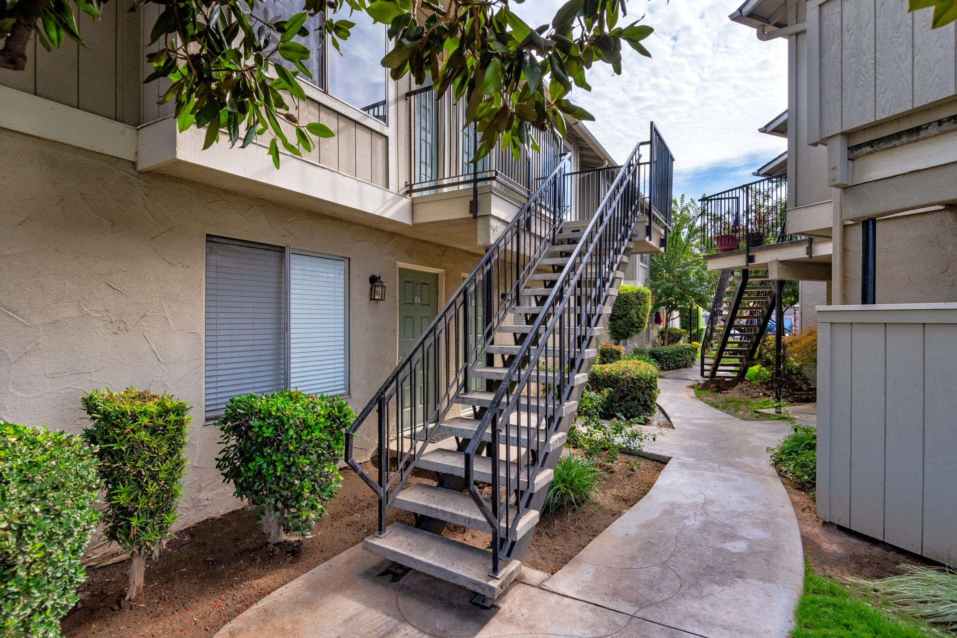 Exterior of a two-story apartment building with stairs, a pathway, and landscaping.