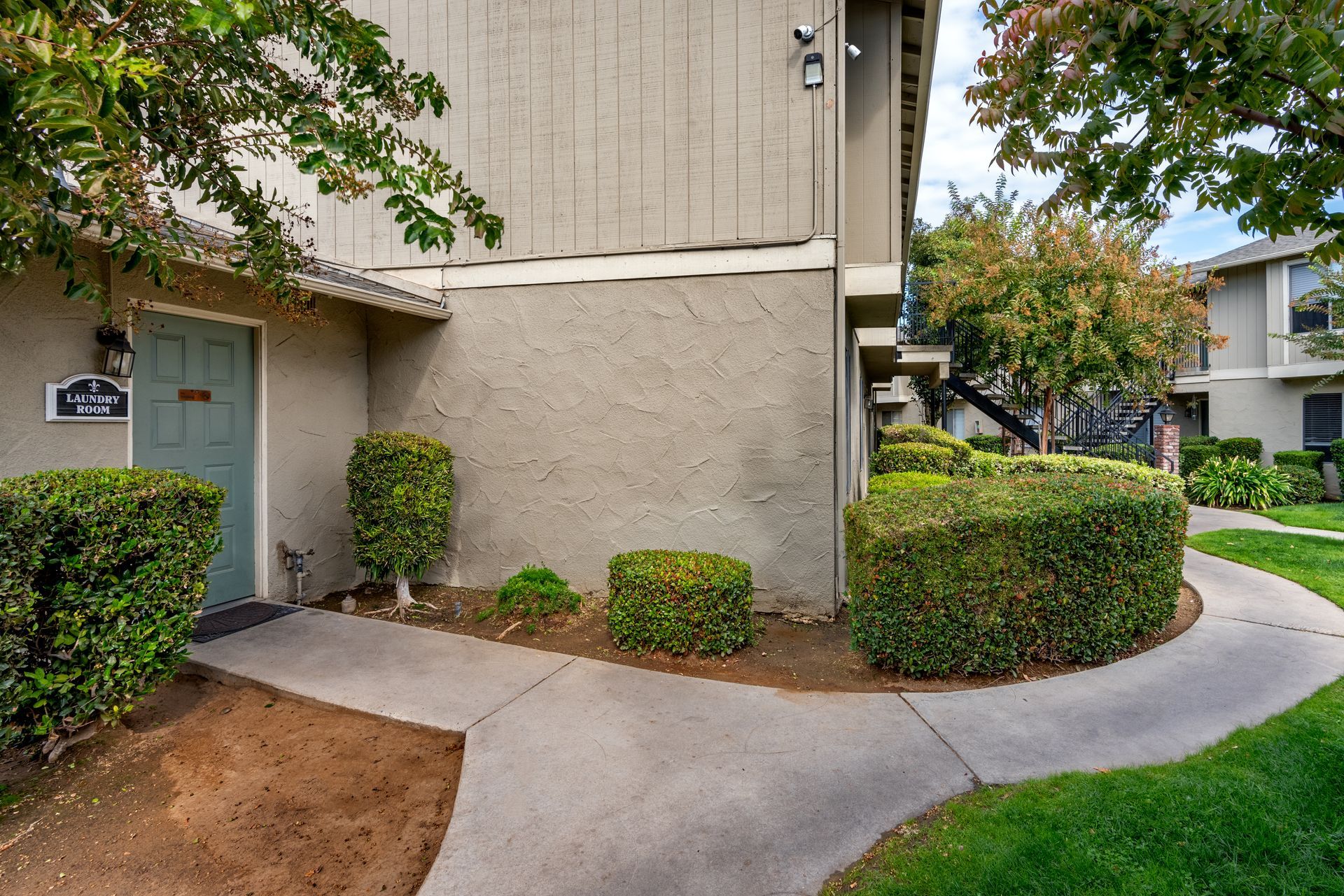Exterior view of beige apartment building with walkway and trimmed bushes.