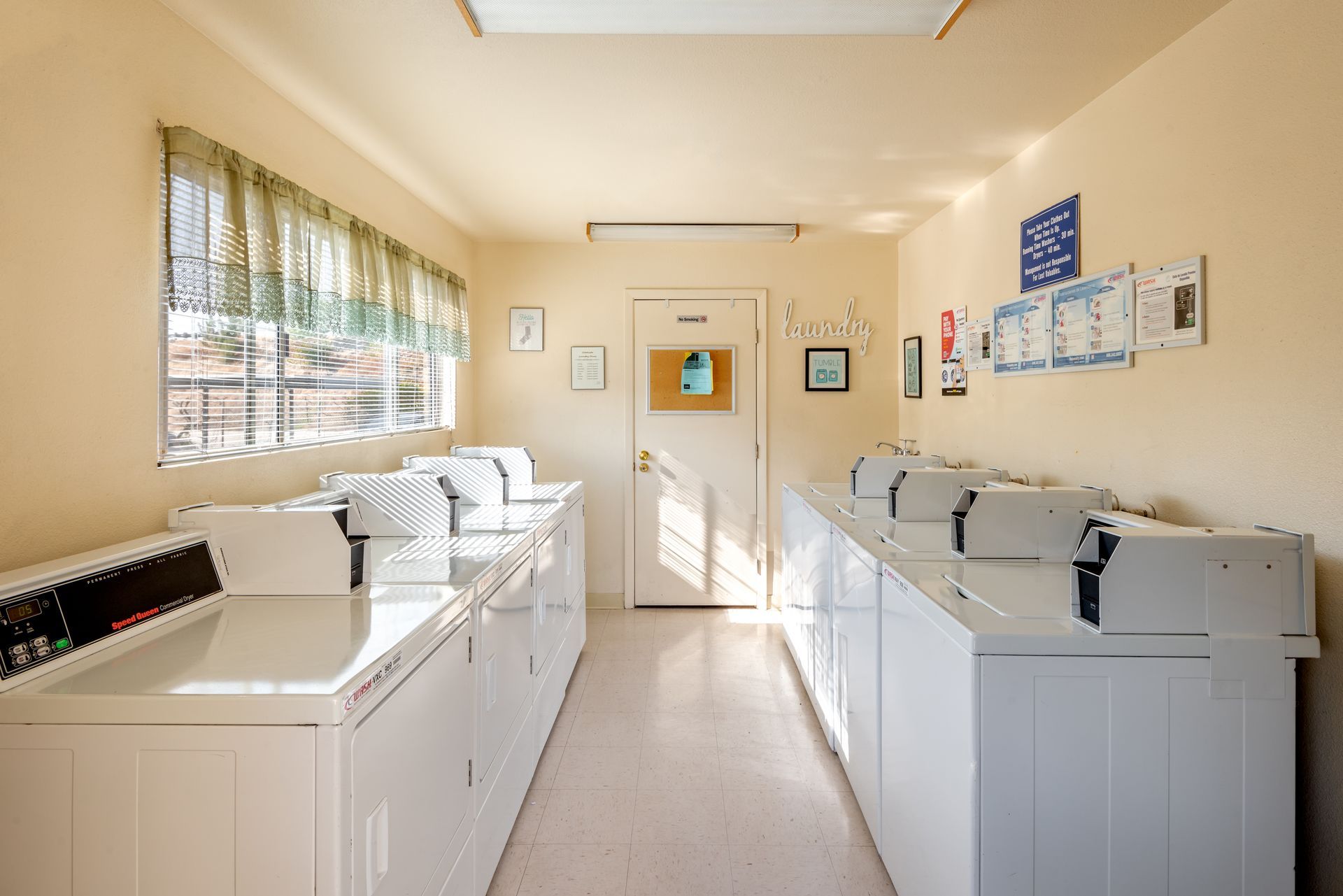 Laundry room with rows of white washing machines, a window, and a door.