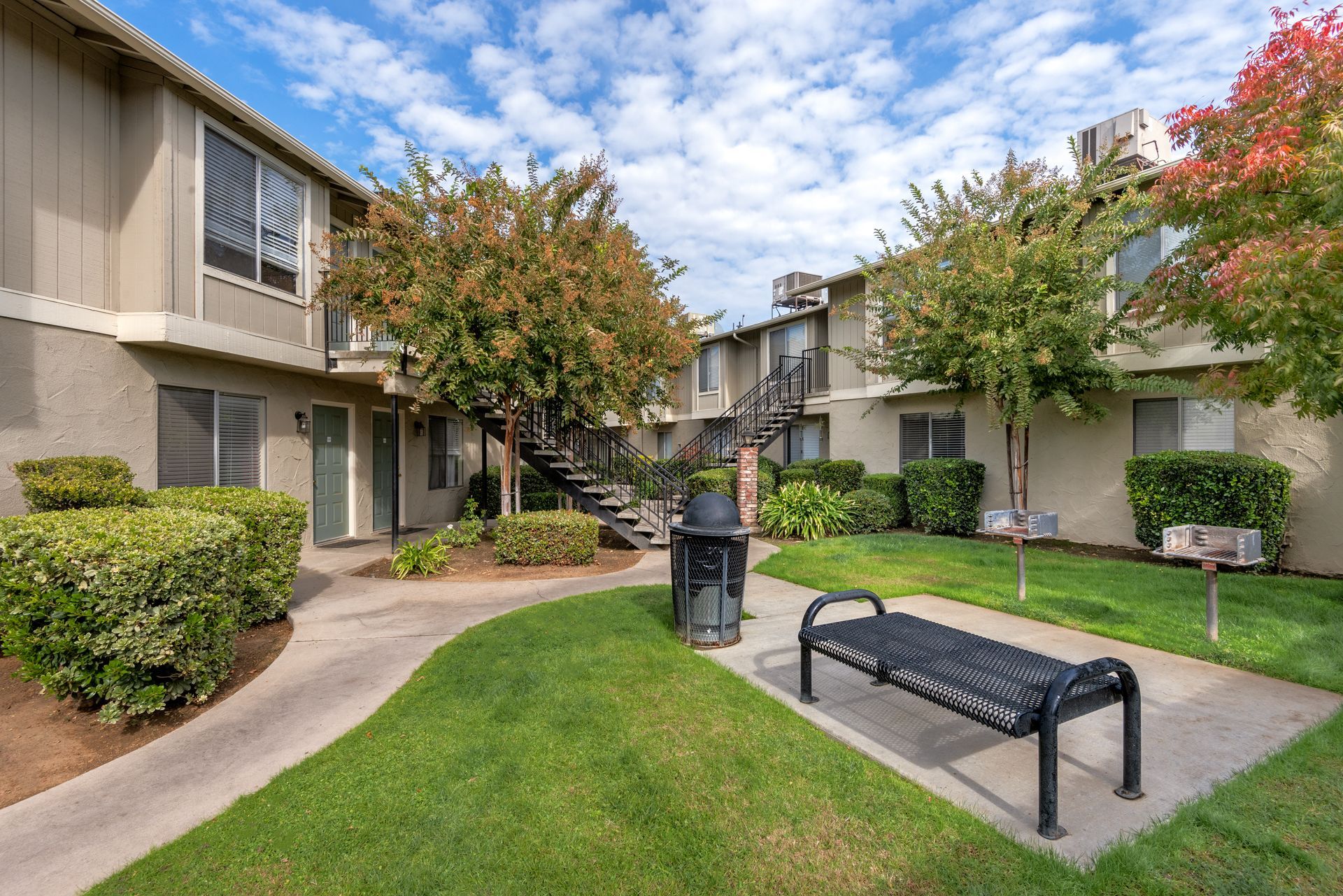 Apartment complex courtyard with green grass, a bench, and walkways. Overcast day.