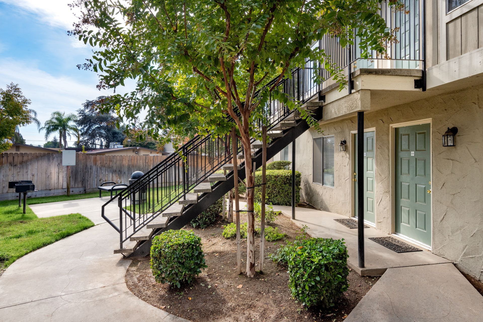 Apartment complex exterior with stairs, green doors, and a small tree.