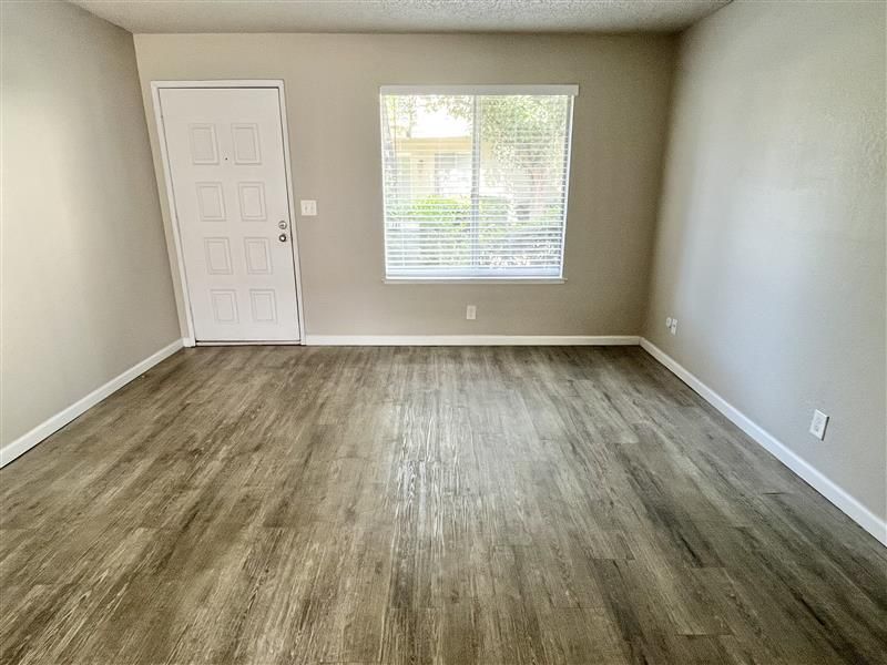 Empty room with wooden floor, white door, and window with blinds. Beige walls.