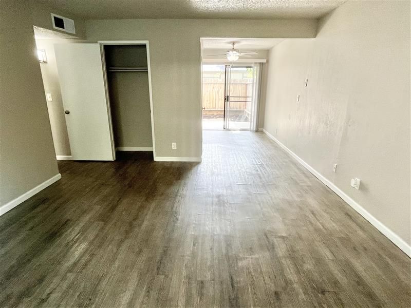 Empty living room with gray walls, wood-look flooring, closet, and a sliding door to a patio.