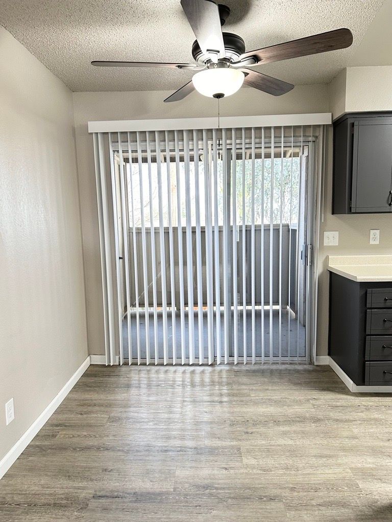 Interior view with sliding glass door and vertical blinds, ceiling fan, and kitchen cabinets.