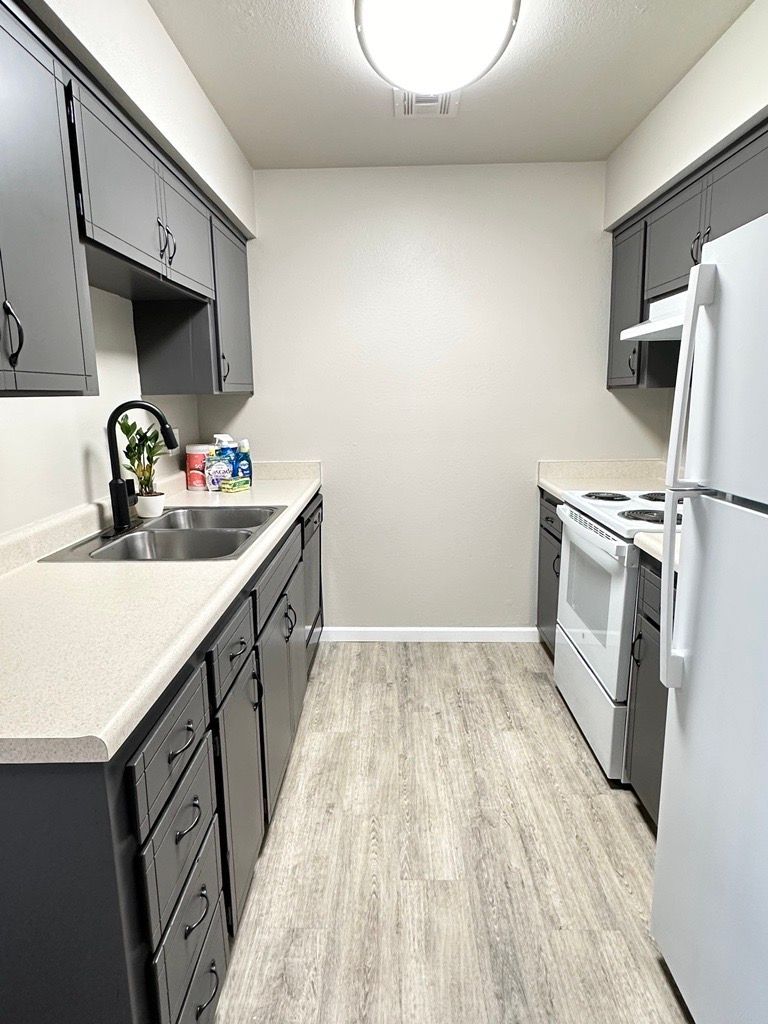 A galley kitchen with gray cabinets, white appliances, light countertops, and wood-look flooring.