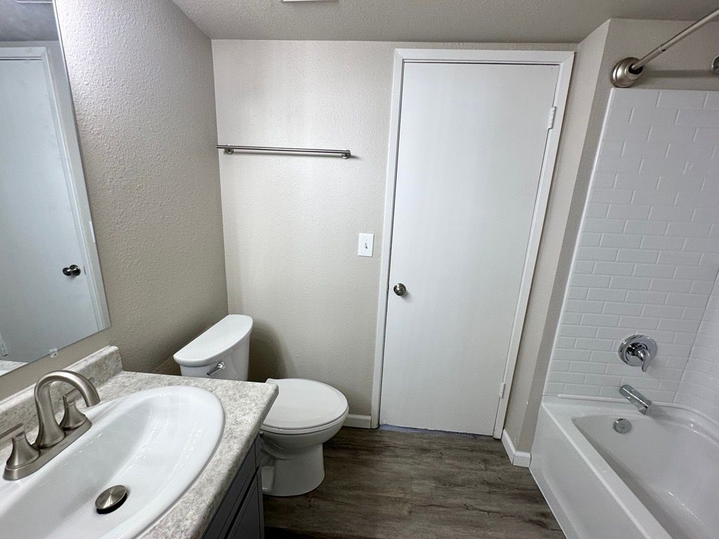Bathroom with a sink, toilet, door, and tub/shower. Light gray walls and floor.