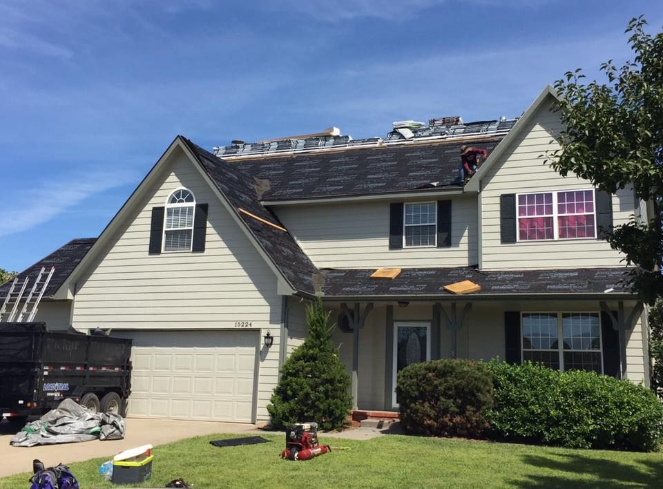 House with roof being repaired on a sunny day; a truck and tools are visible in the yard.