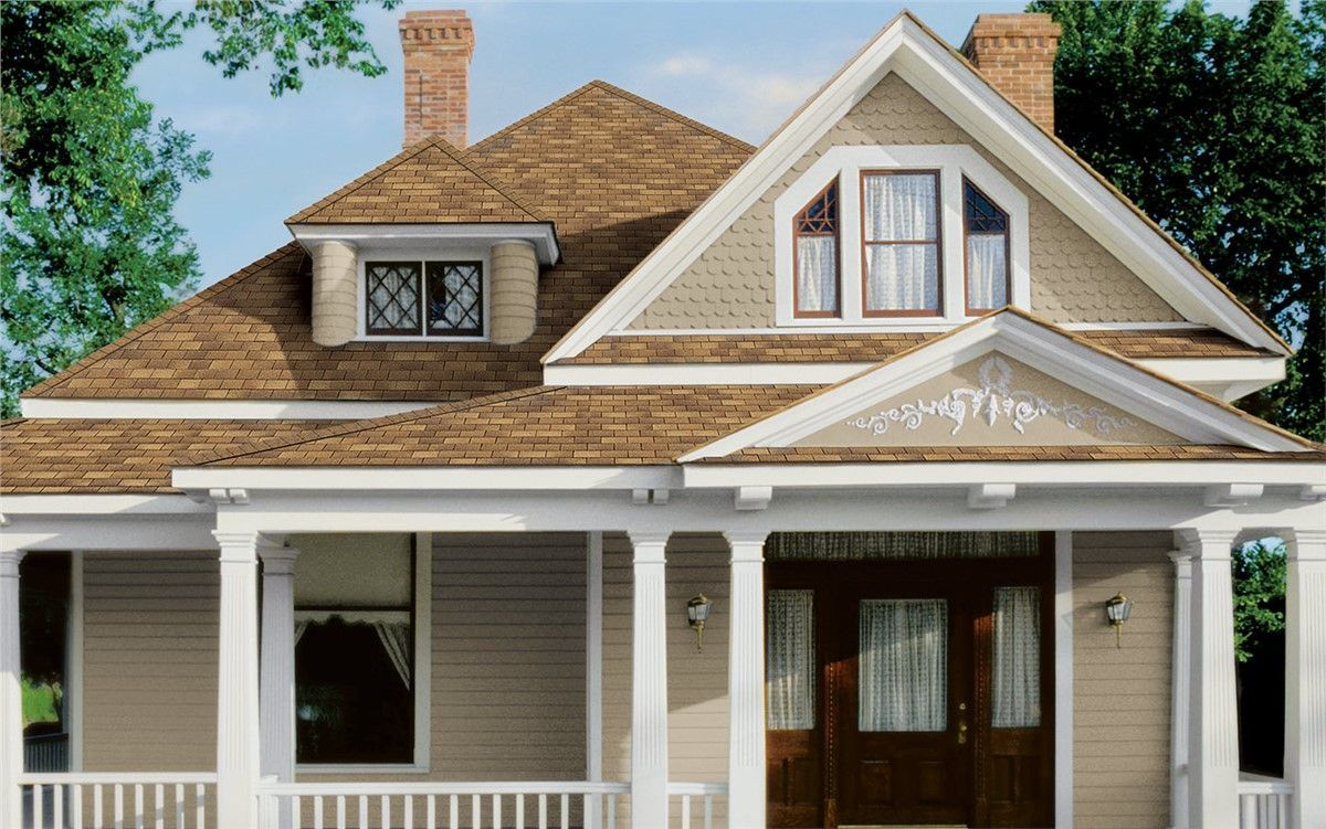 Tan and brown Victorian house with porch, gable, and two chimneys, framed by trees.