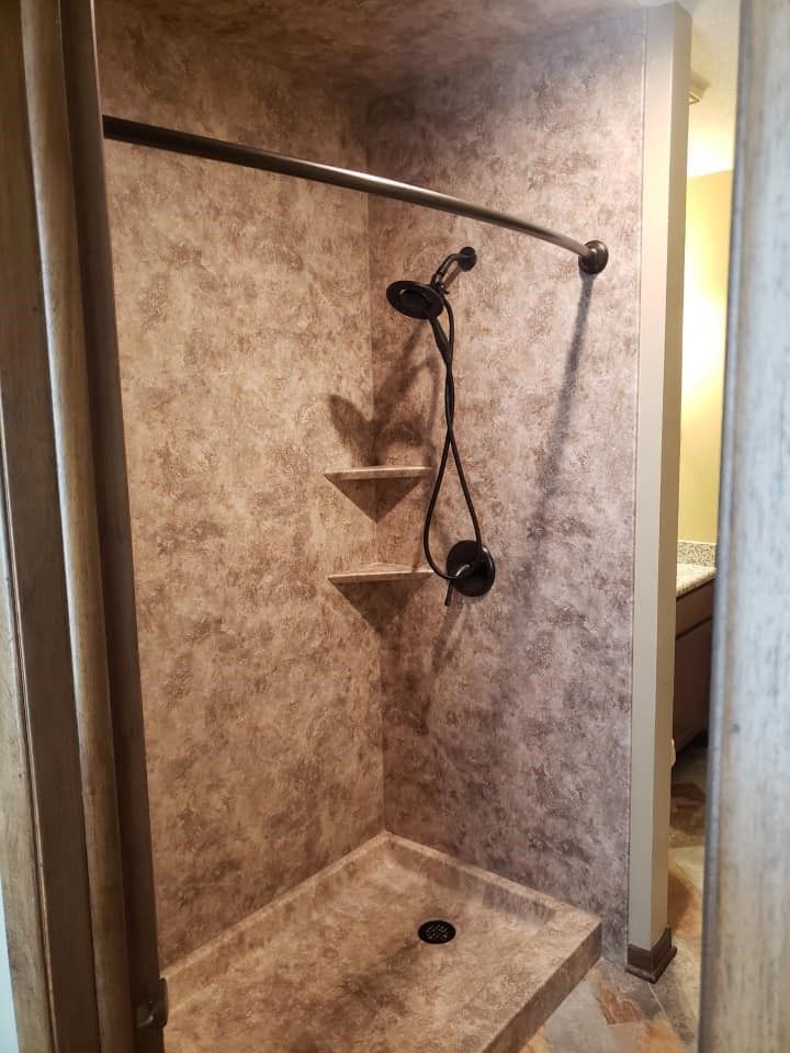 Small shower stall with dark fixtures and textured beige walls.
