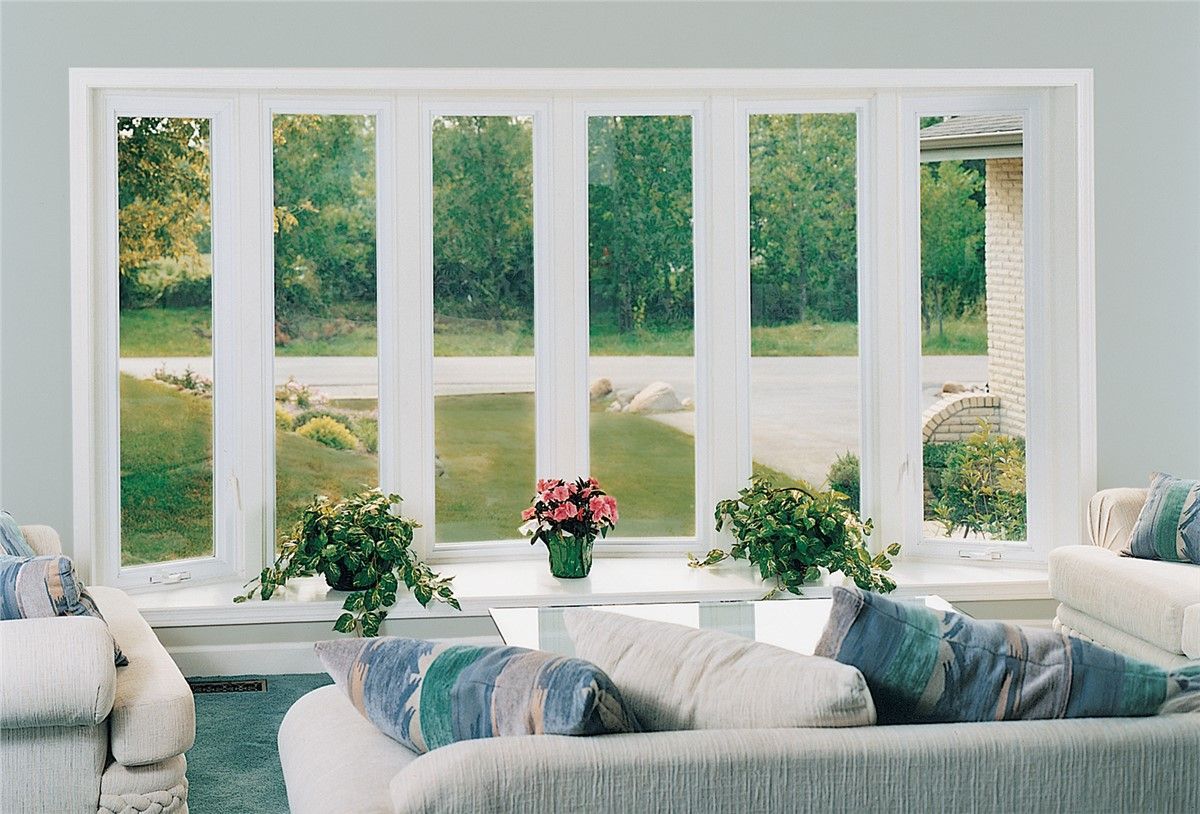 Living room with large white windows overlooking a garden. A couch and plants are in front of the windows.