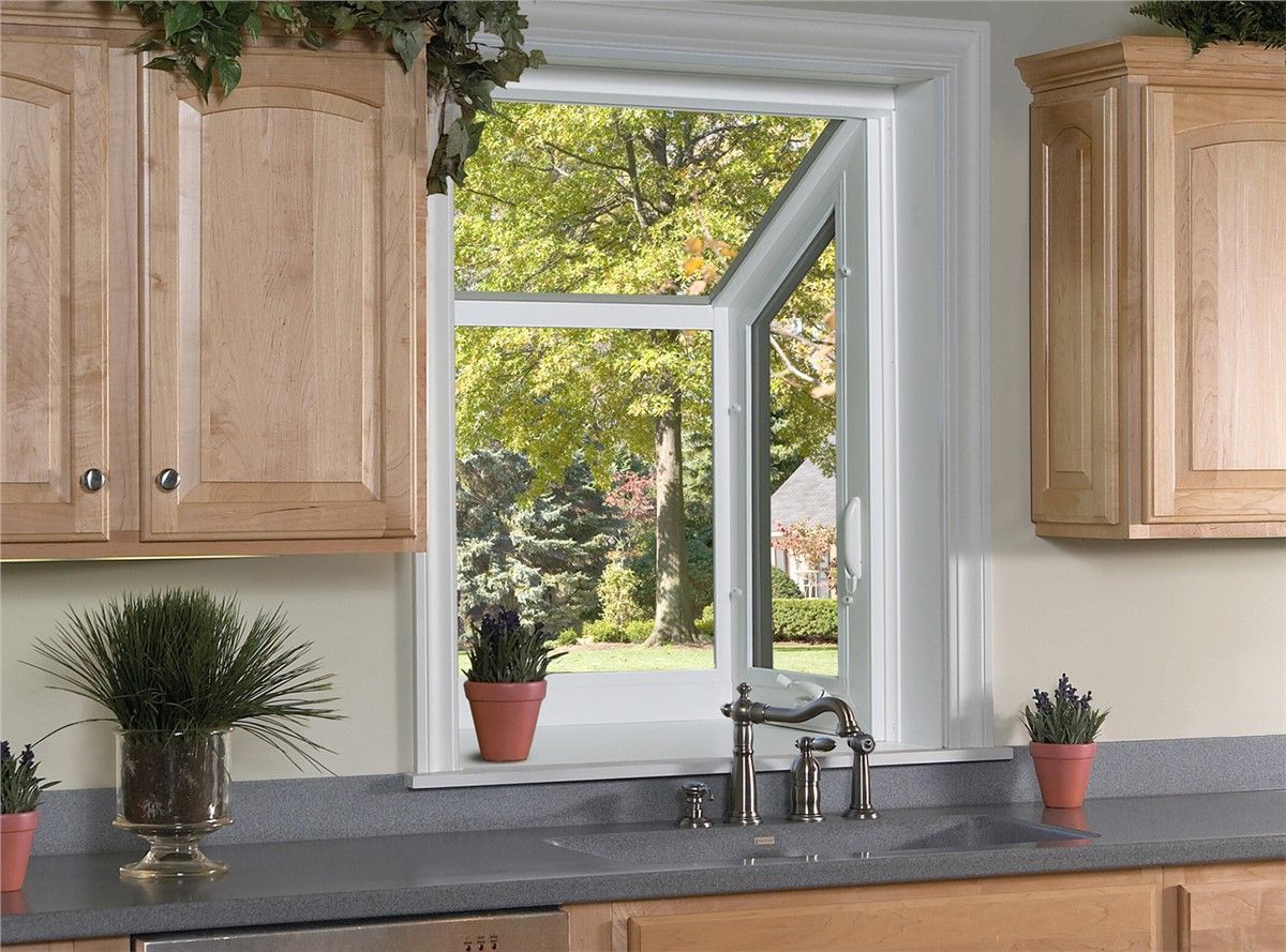 Kitchen with open window. Light wood cabinets, gray countertop, sink, and potted plants. Lush green trees outside.