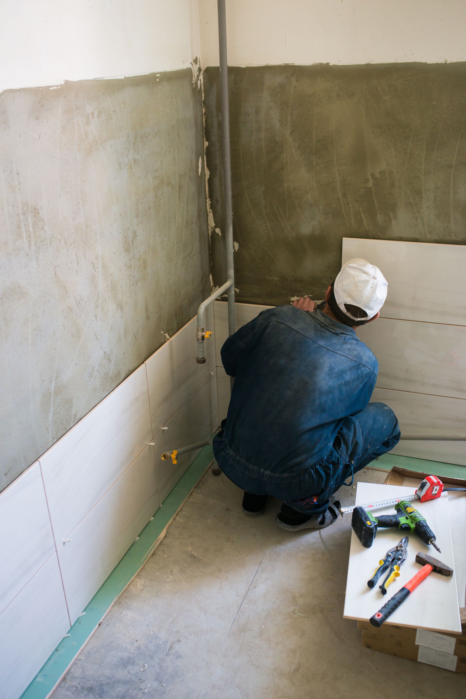 A man is engaged in bathroom remodeling services, applying tiles to the wall for an updated look.