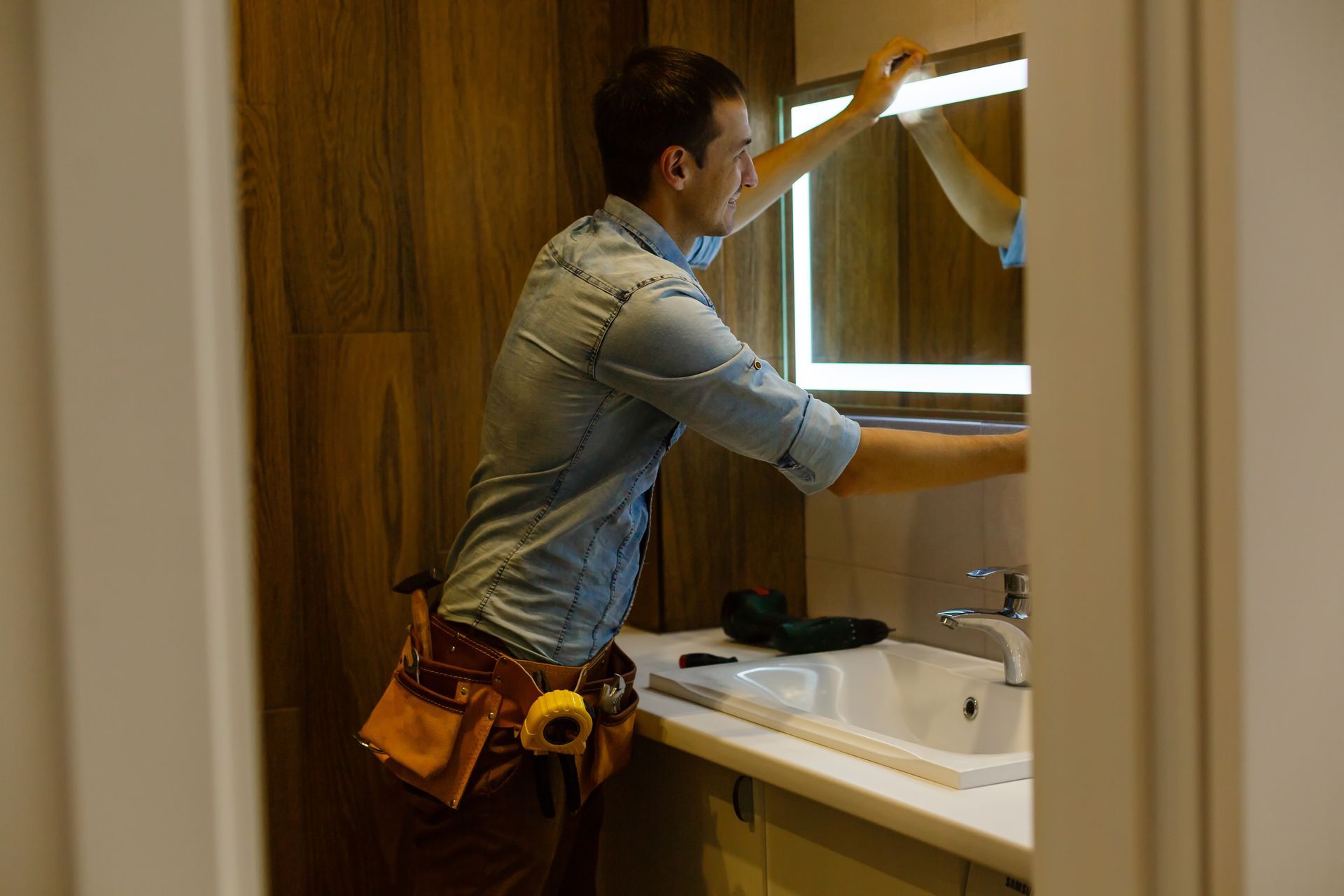 Man mounts mirror in newly renovated bathroom.