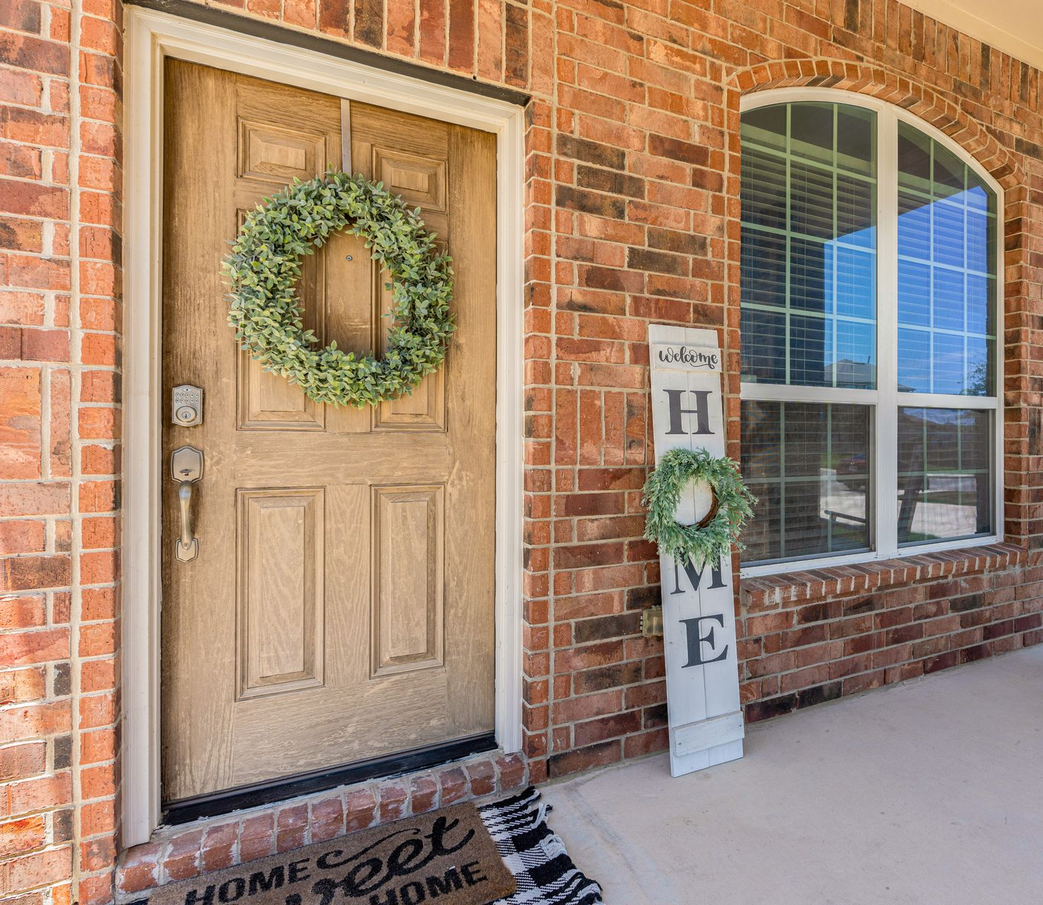 Bathroom with a tub, vanity, and a large window overlooking a yard. Beige walls, wooden cabinets, and brown fixtures.